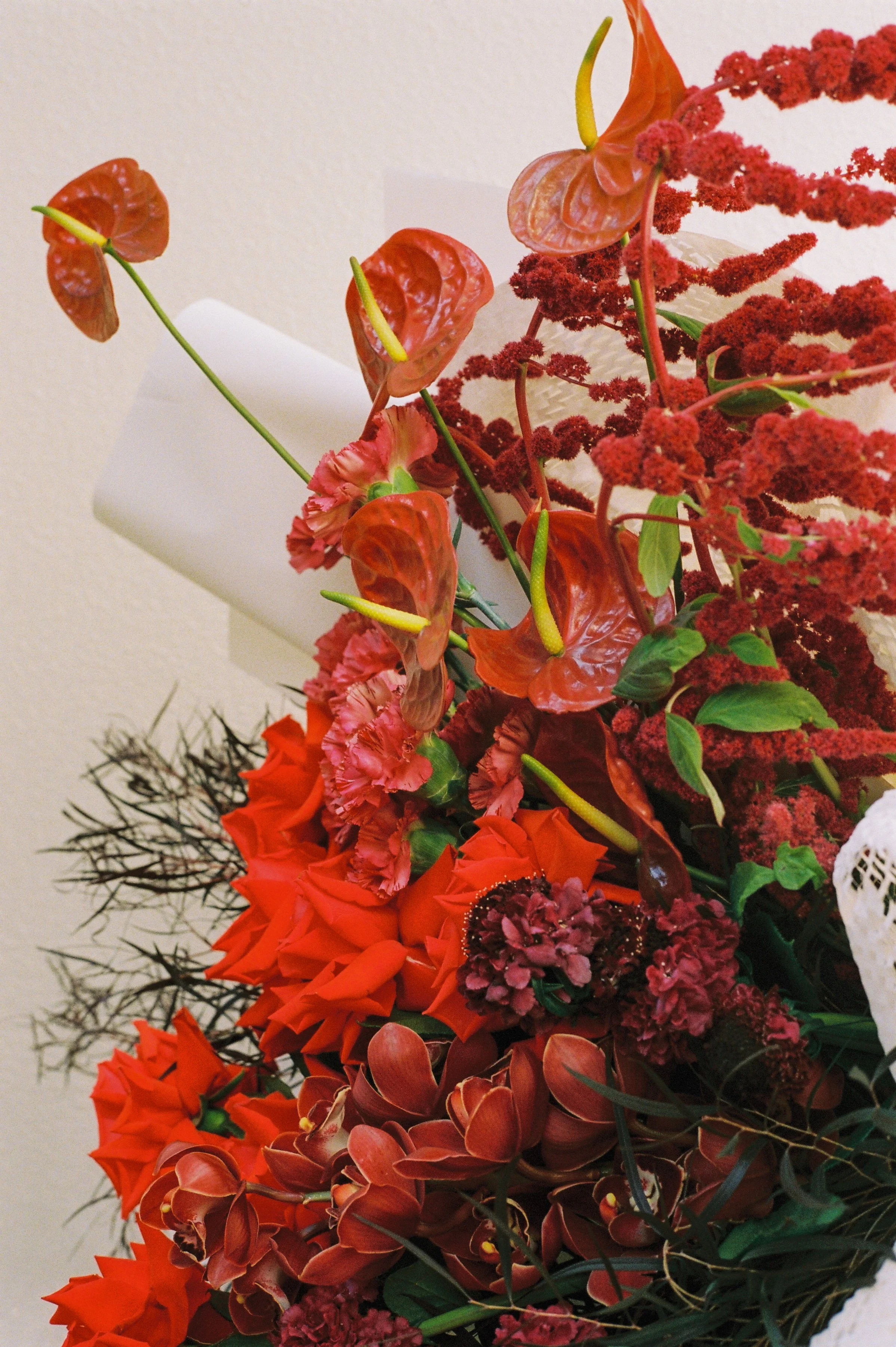 A colorful bouquet of various flowers, including red anthuriums and orange flowers, arranged against a light background.