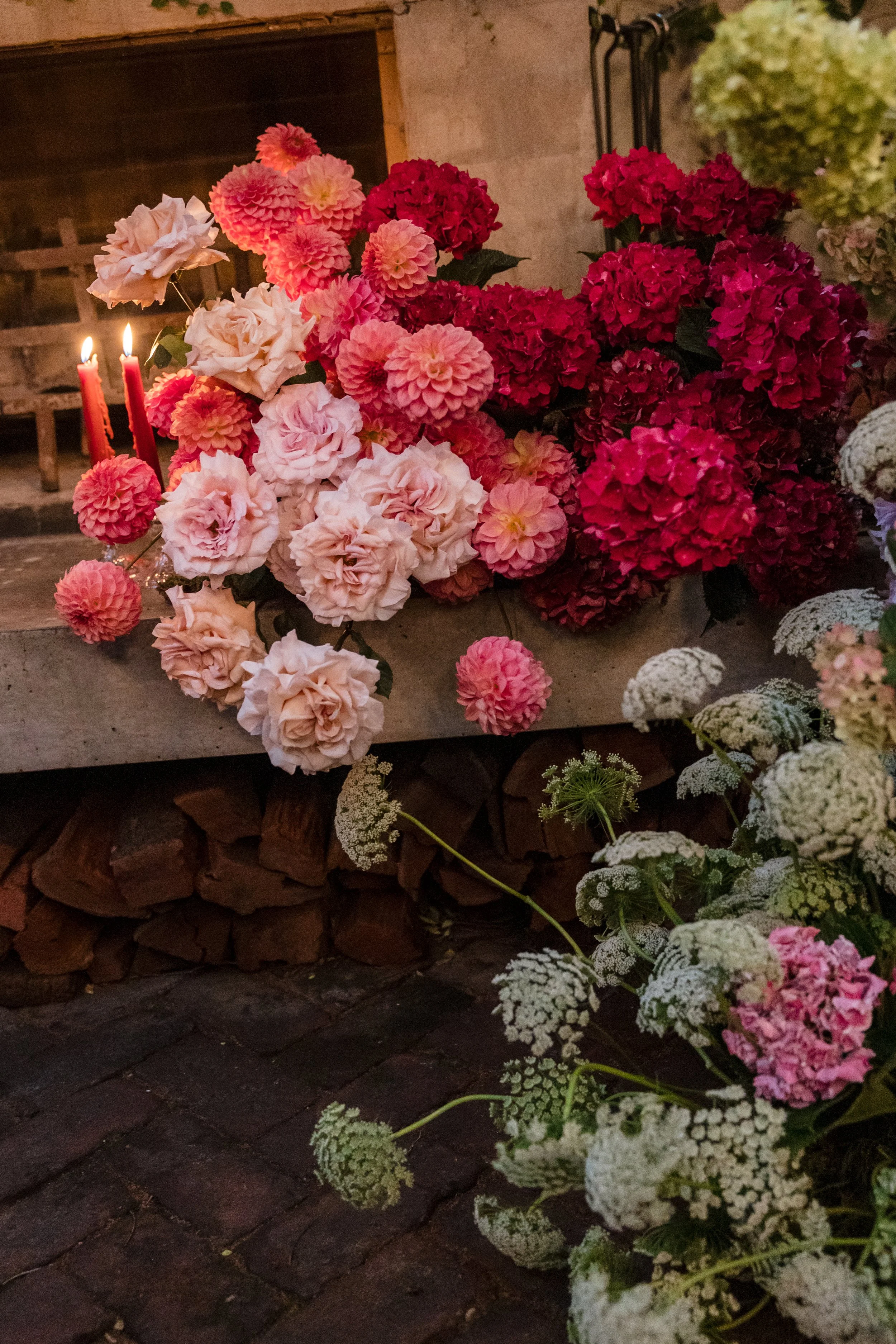 Various pink and red hydrangea flowers and white flowers on a brick speaker, with a candle in the background.