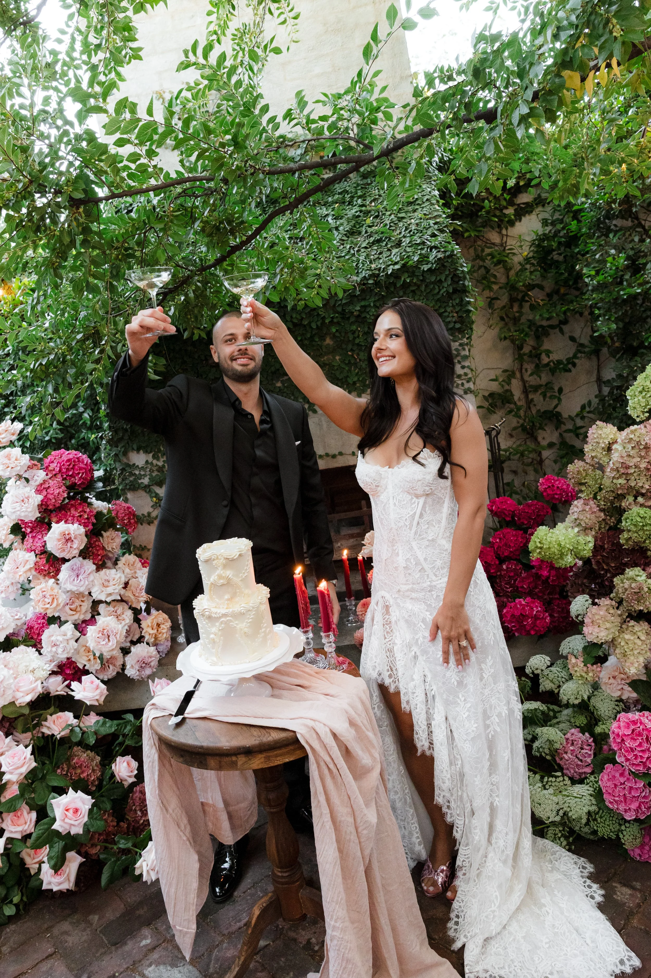 A bride and groom celebrating their wedding, raising glasses in a toast, surrounded by colorful flowers and greenery.