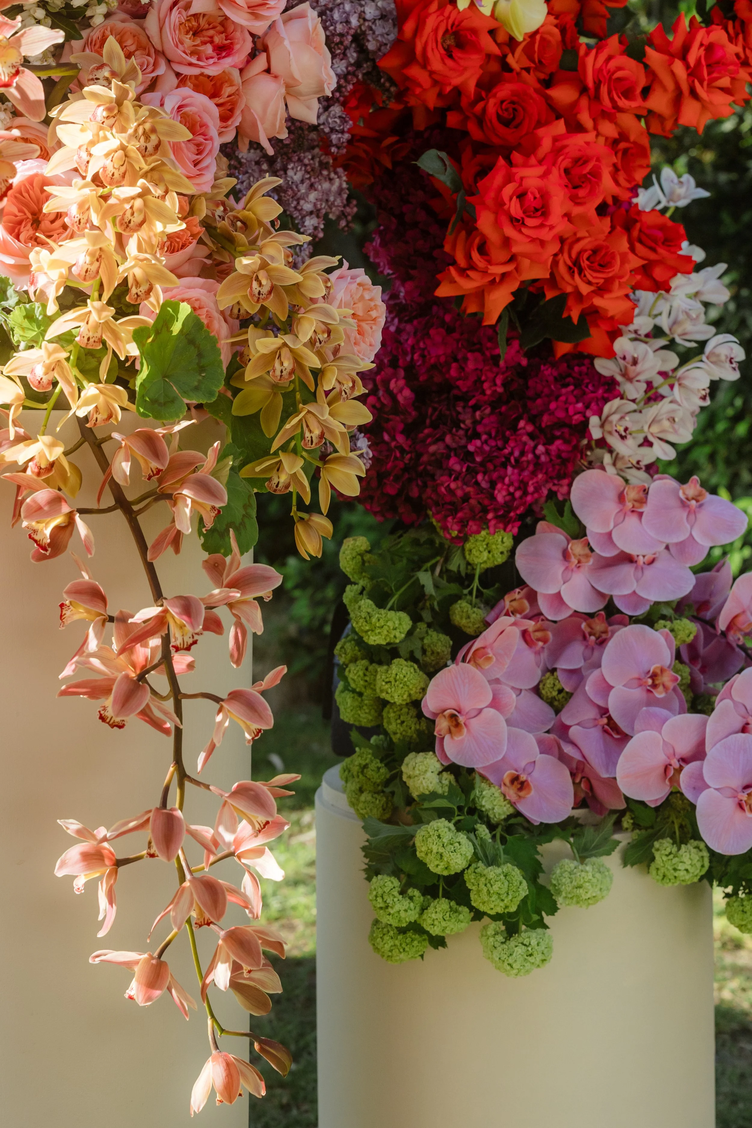 A close-up of various colorful flower arrangements with pink, orange, white, and green flowers, including orchids, roses, and hydrangeas.