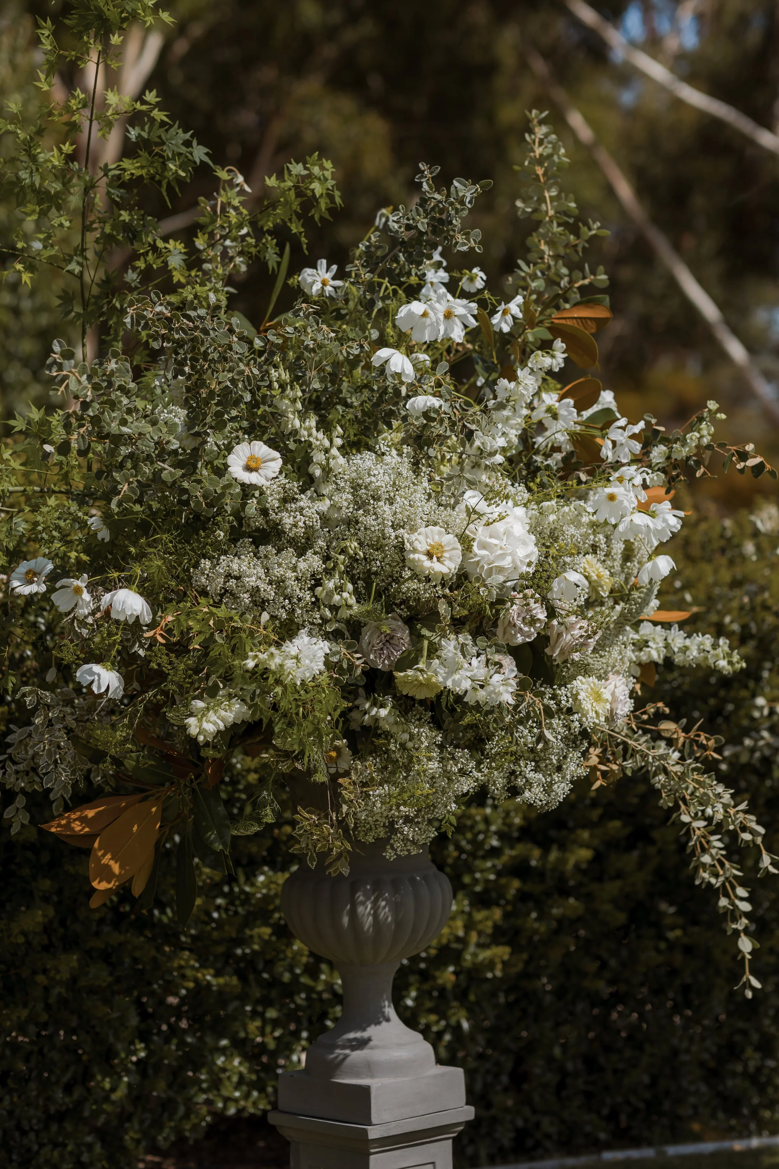 A large floral arrangement with white flowers and greenery in a gray urn.
