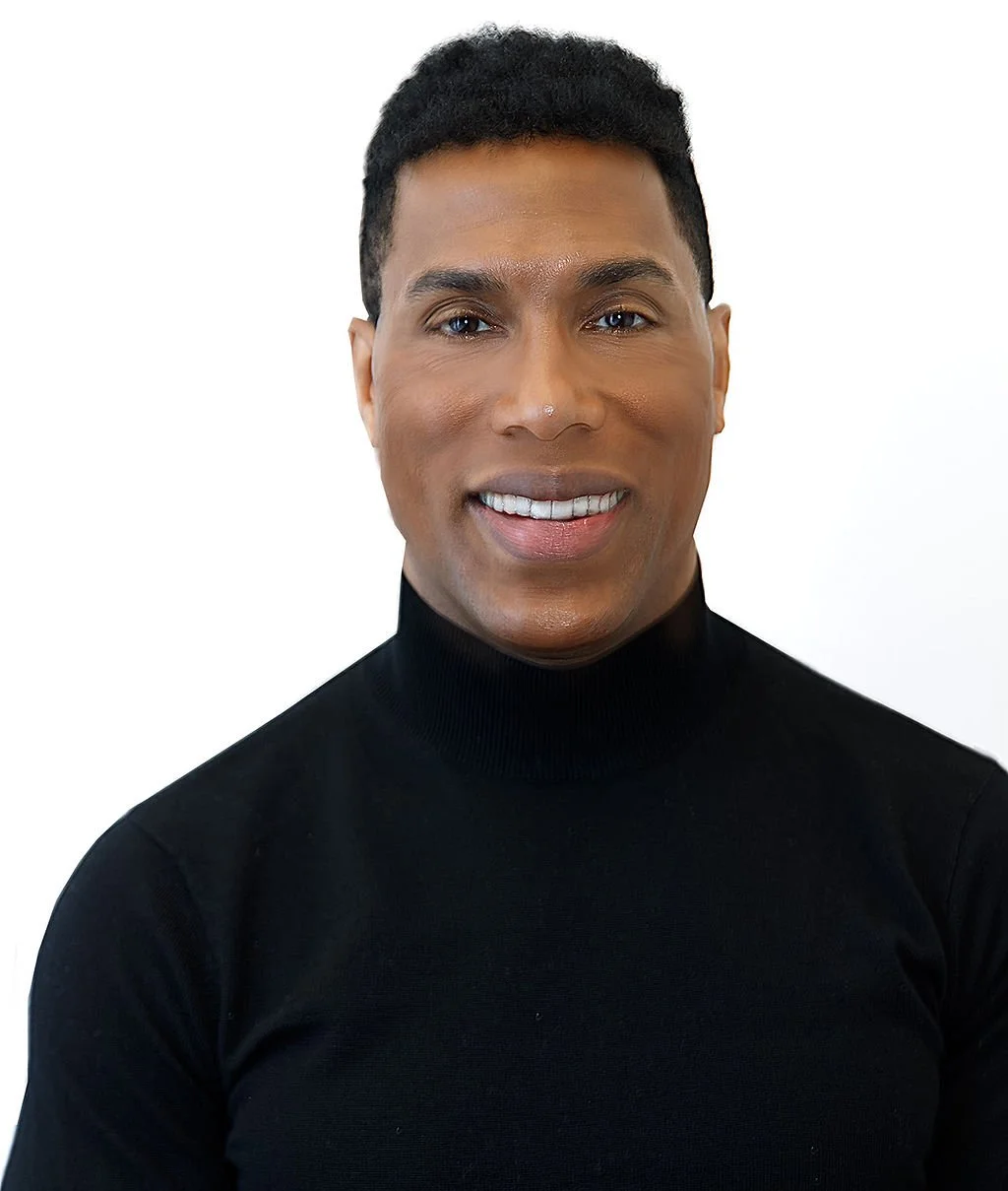 A person with short black hair wearing a black turtleneck sweater, smiling against a plain white background.