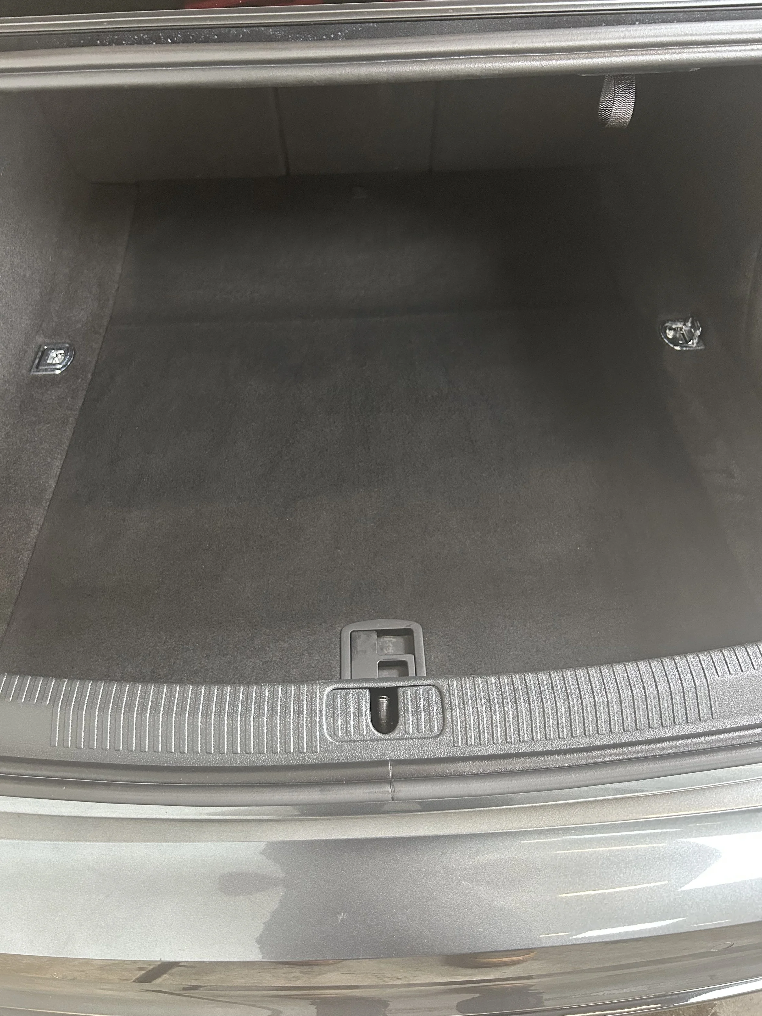 After detailing — freshly cleaned car trunk with dark carpeting, no debris, and metal hooks visible on the sides.