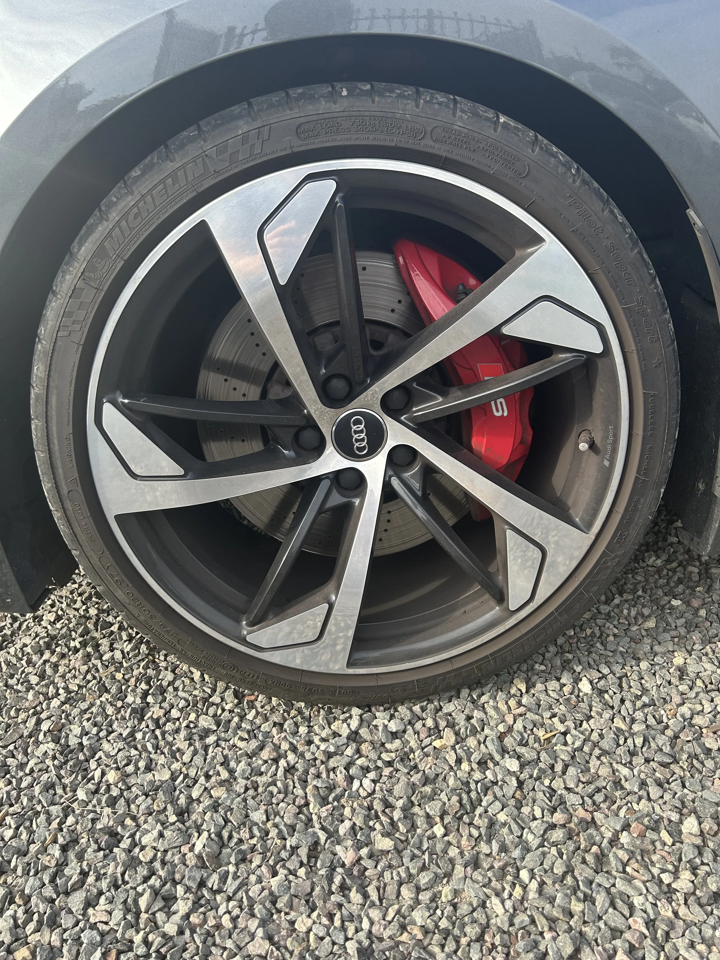 Before detail – close-up of a car wheel with an Audi rim and red brake caliper, showing dirt and brake dust buildup on the spokes and surrounding area.