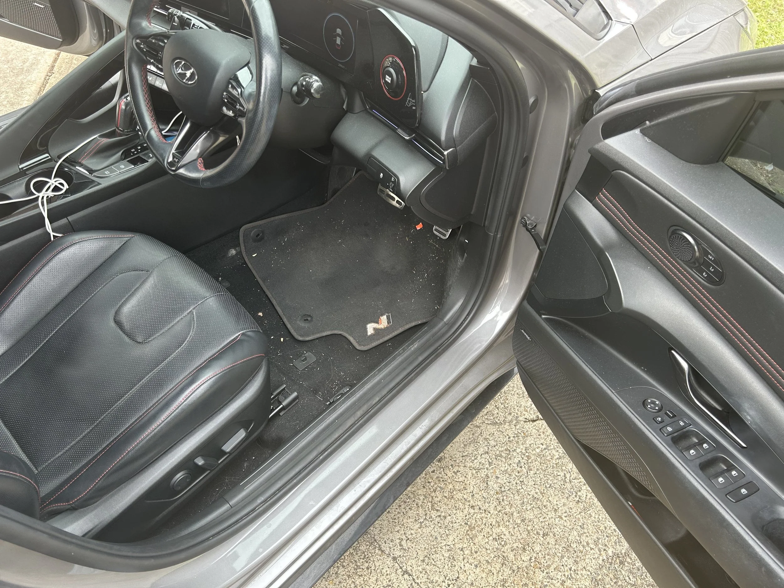 Before car interior detail showing dirty driver’s seat area, pedals, dashboard and door panel with visible debris and grime.