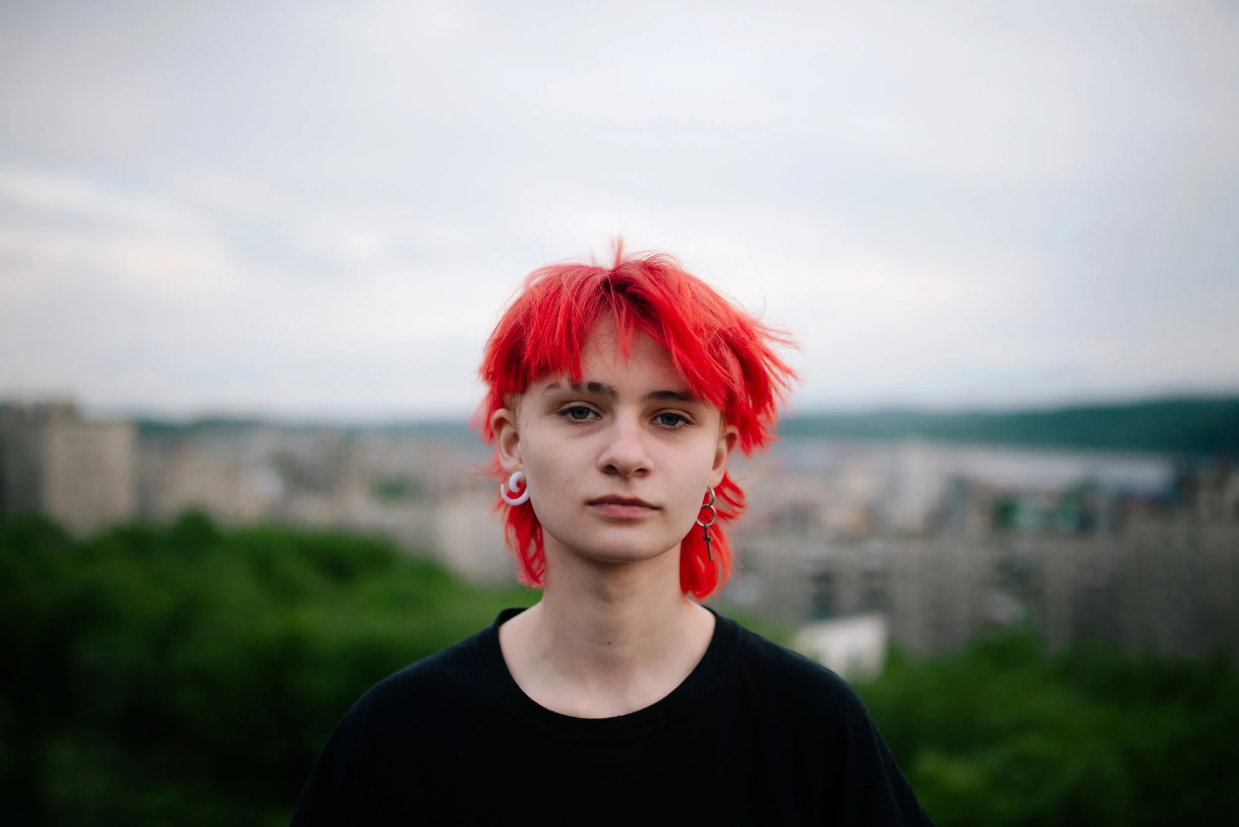 Portrait of red-haired teenager against a blurred cityscape in Russia. Photograph by Semyon Kokorin featured in “Semyon’s World” by Timofey Abel.