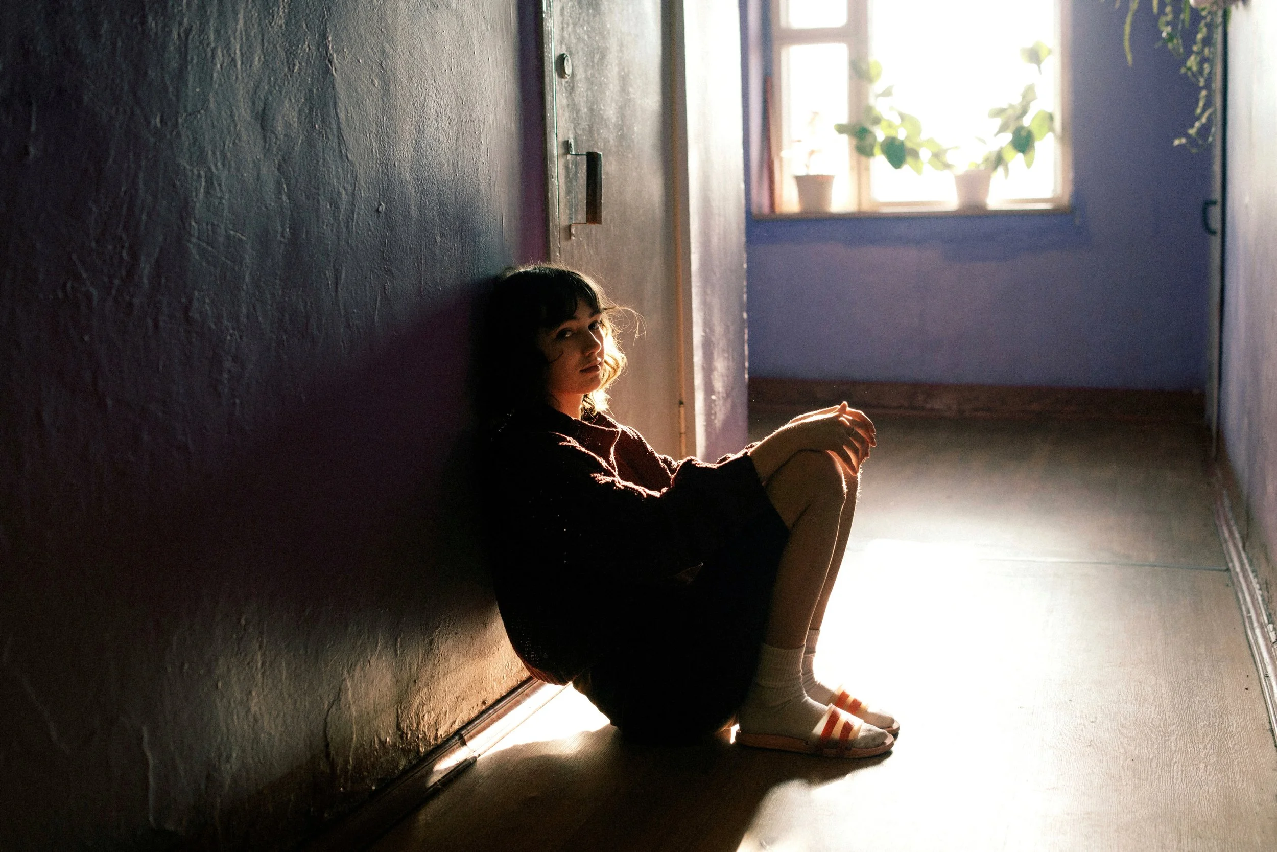 Young woman sitting alone in a hallway lit by afternoon sunlight in Russia. Photograph by Semyon Kokorin featured in “Semyon’s World” by Timofey Abel.
