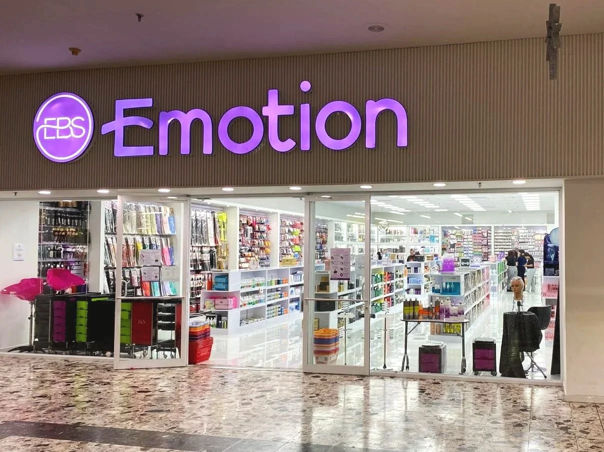 Storefront with purple signage that reads 'EBS Emotion', featuring glass doors revealing stationery supplies and organized shelves inside.