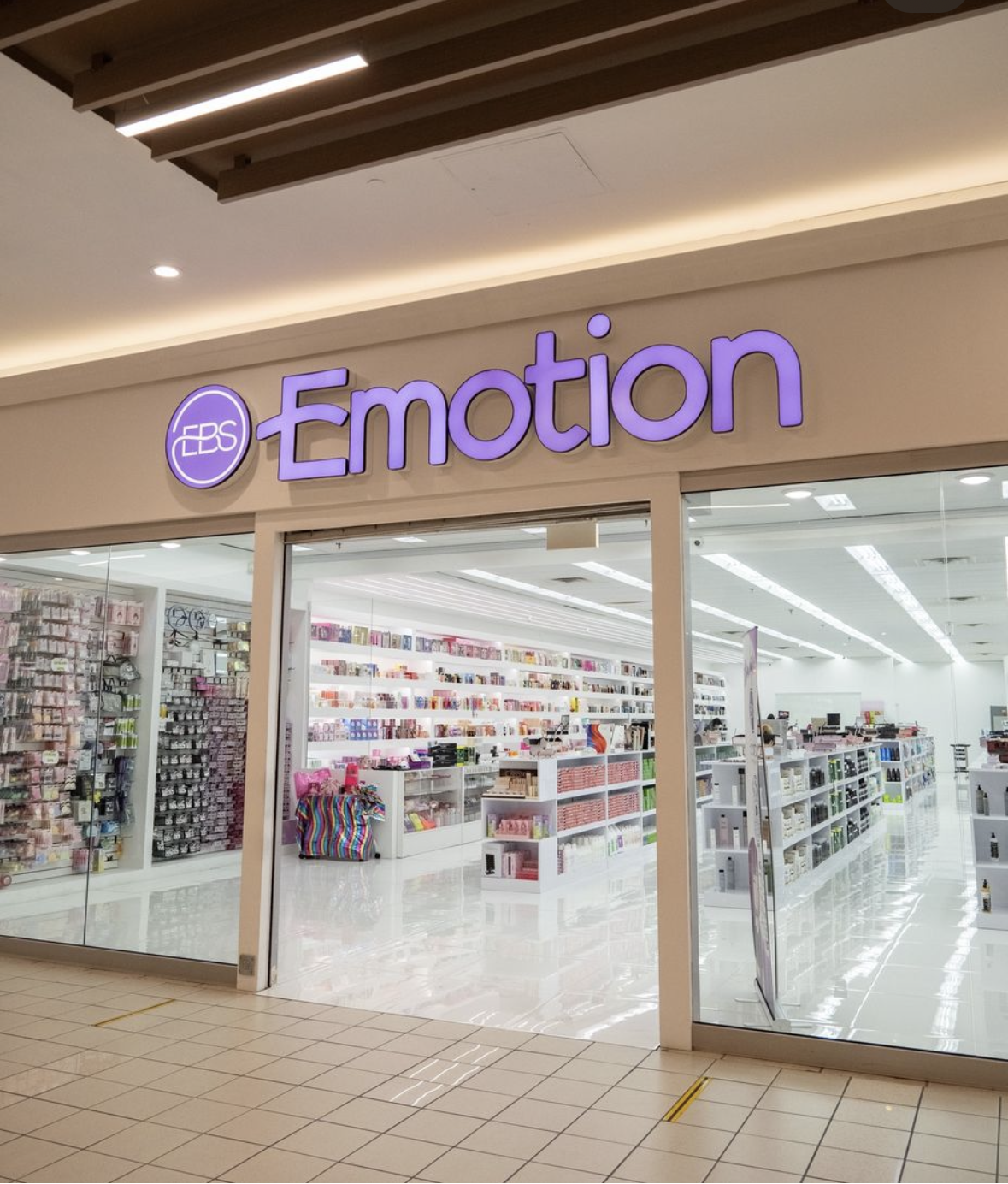 Storefront with purple neon sign that reads 'EBBS Emotion' in a shopping mall, showing an interior filled with various colorful products on shelves.