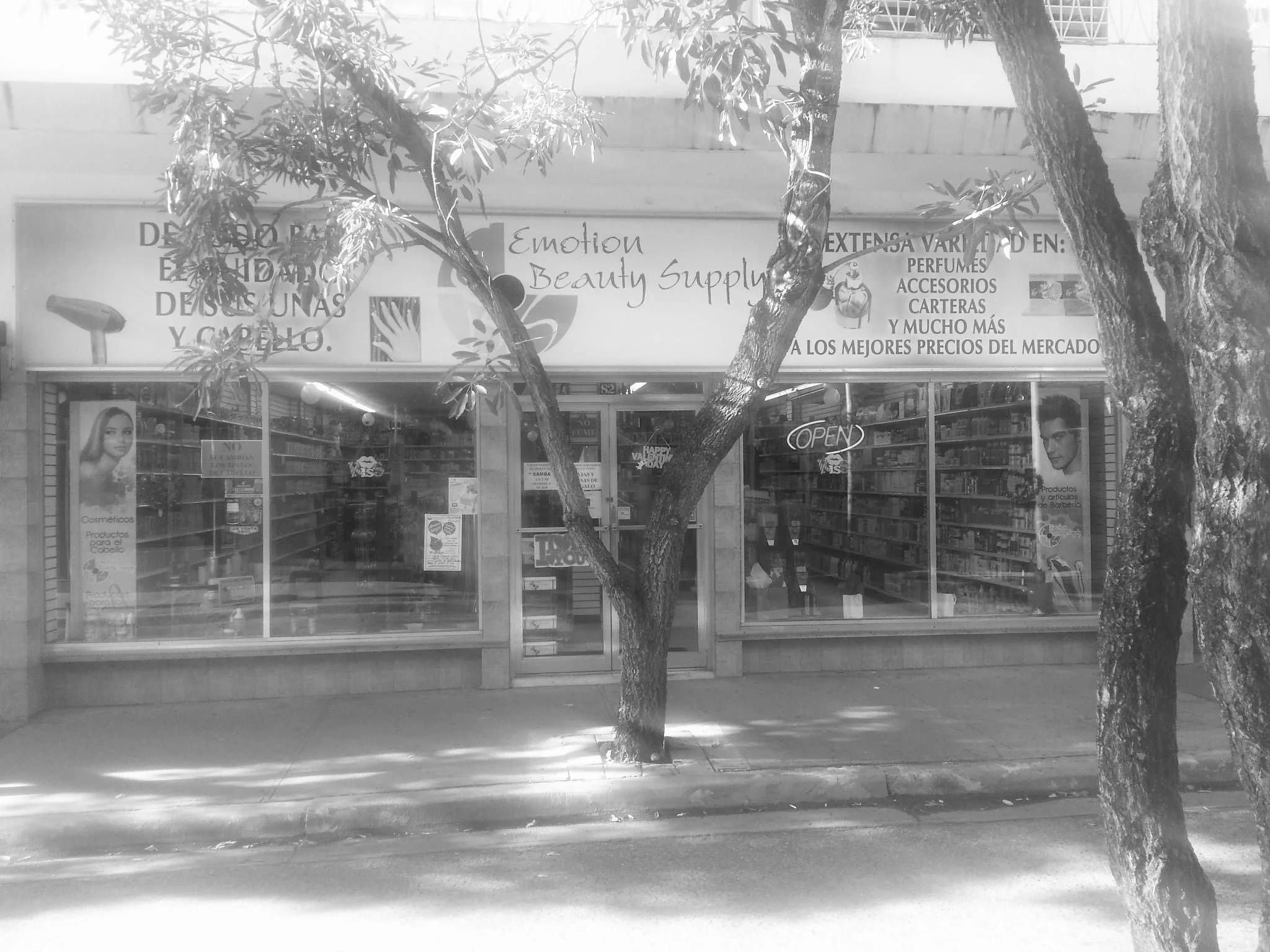 Front view of a small store named 'Emotion Beauty Supply' with large windows displaying products, trees partially obscuring the storefront, and an