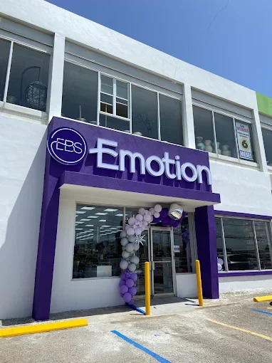 The storefront of a business called Emotion with a purple sign and balloon decoration at the entrance, located in a white building with large windows.