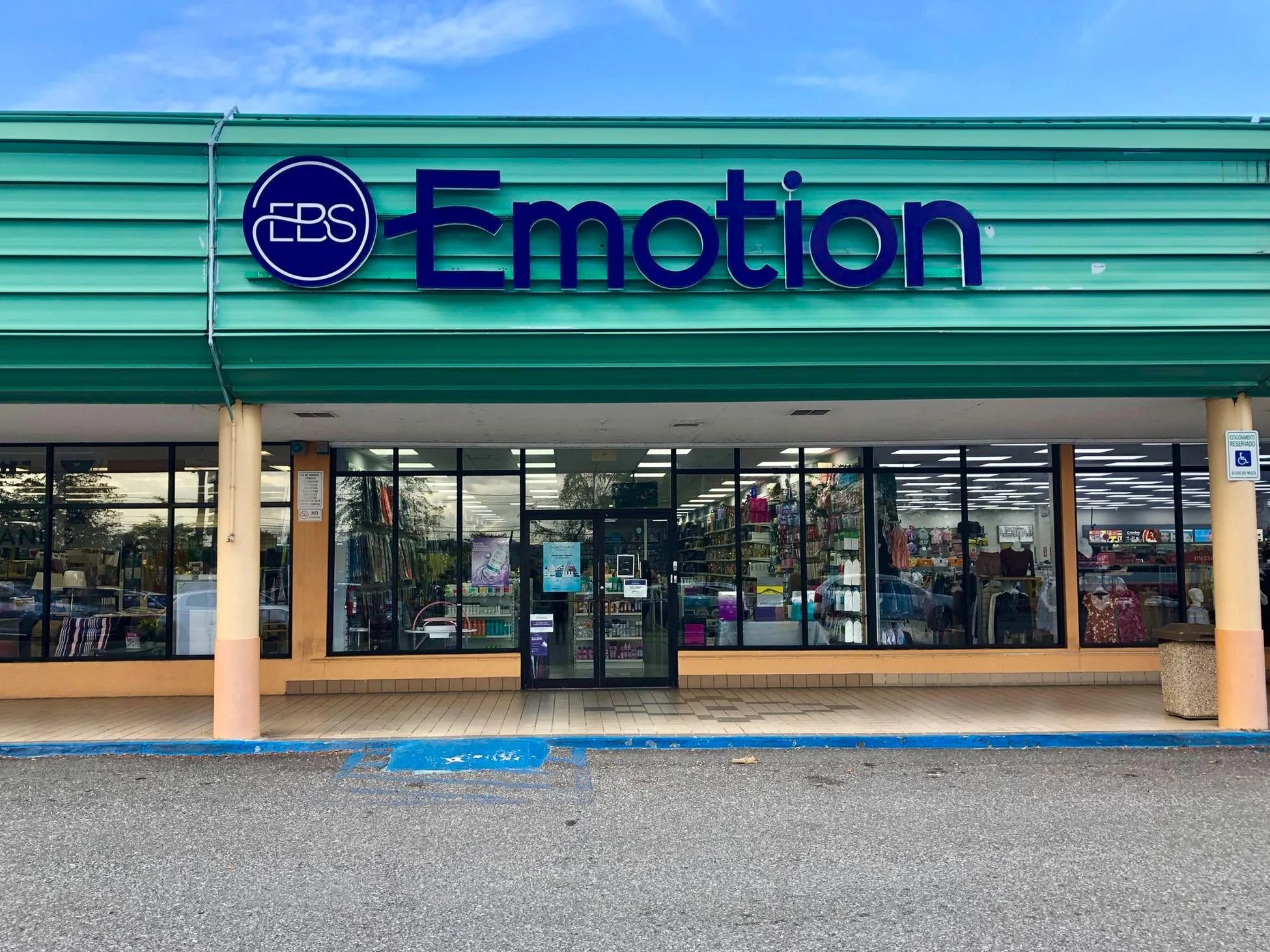 Storefront with a sign reading 'Emotion Beauty Supply & Perfumes' in front of a parking lot with a disabled parking space and cars.