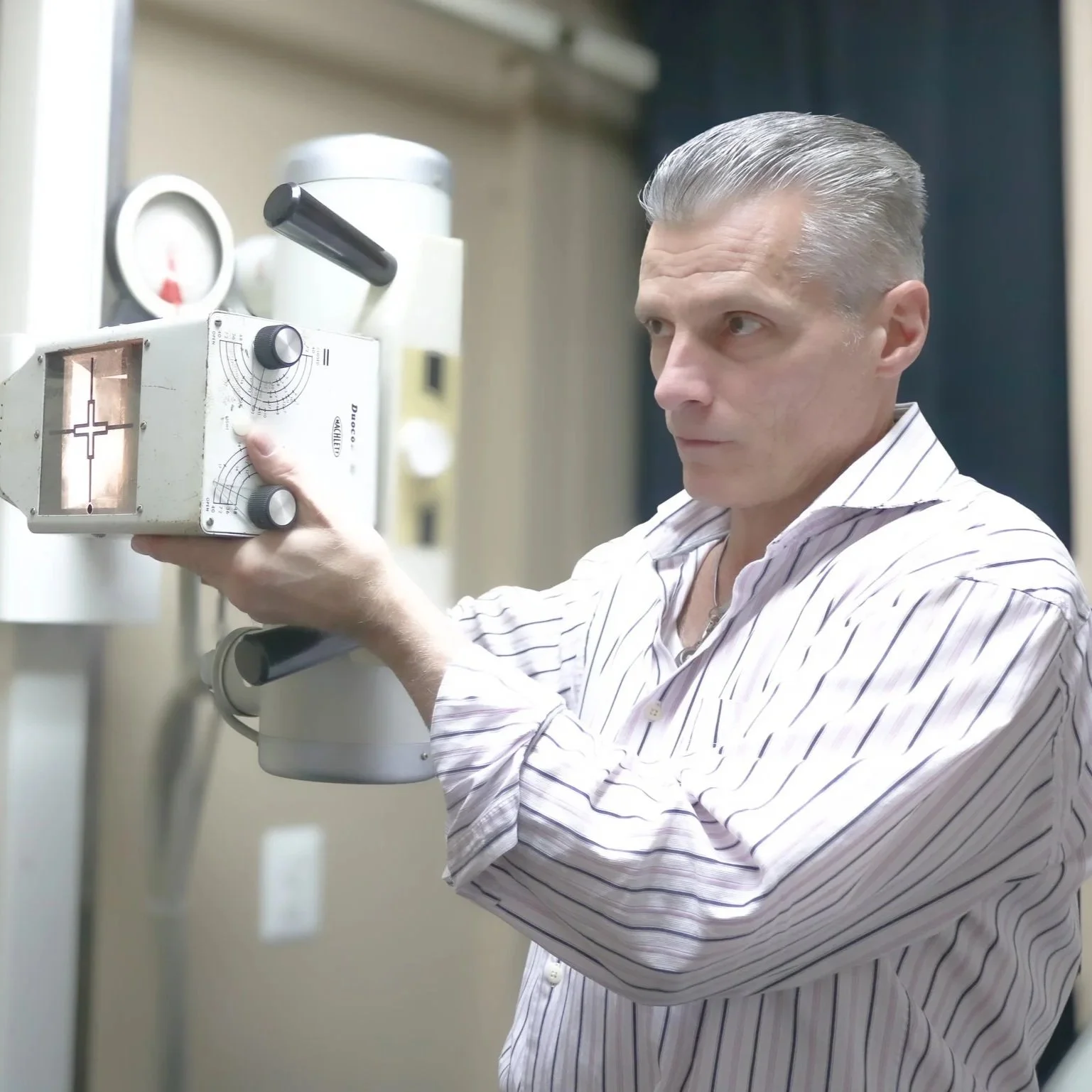 A chiropractor professional with gray hair and a striped shirt operates a piece of scientific equipment, possibly a spectrometer or similar device, in a laboratory setting.