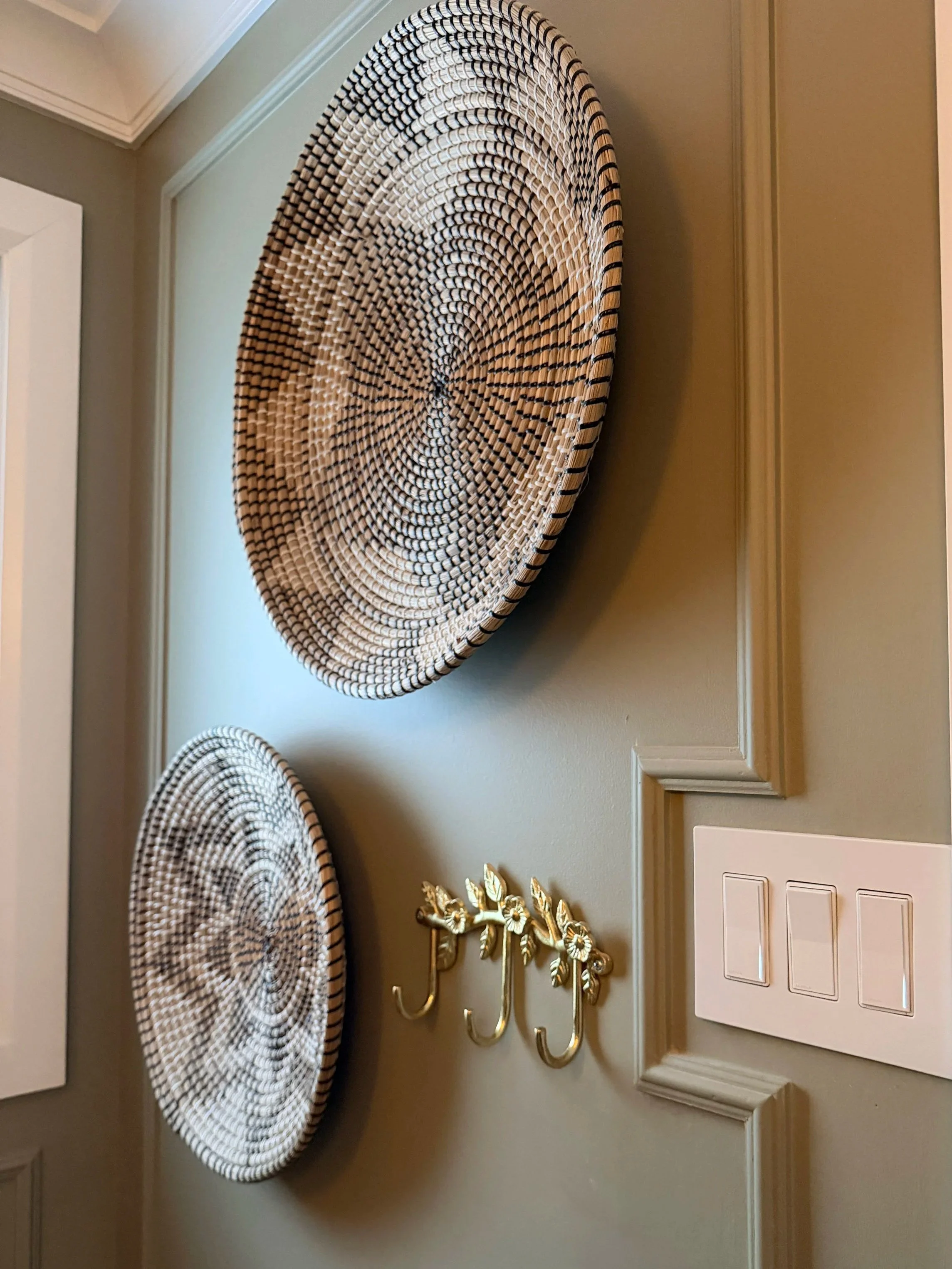 Decorative wall hooks with gold floral design and three umbrellas with black and white striped patterns hanging on a beige wall.