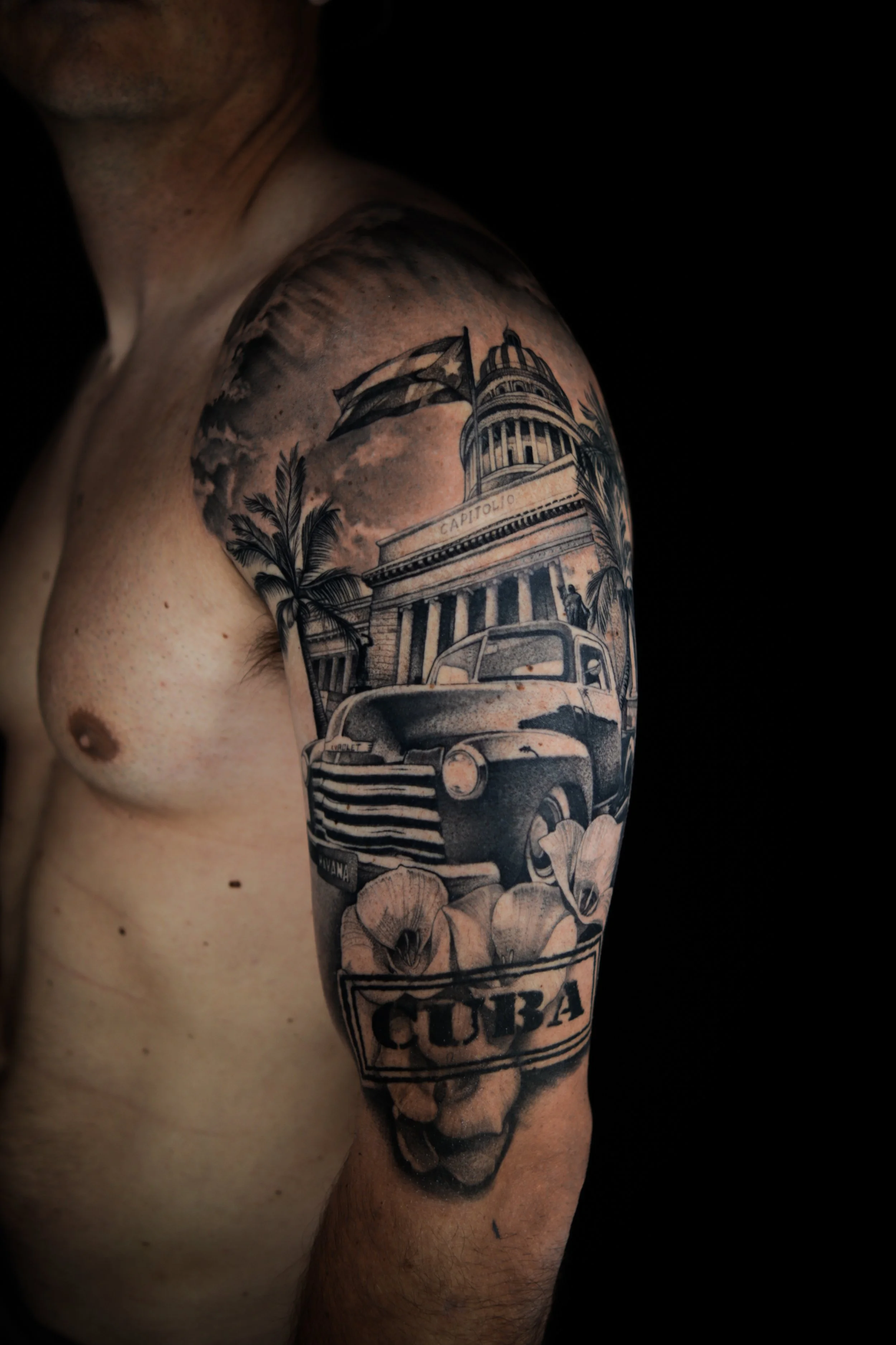Tattoo of a vintage Cuban scene featuring a classic car, a building with the word 'Capitolio,' palm trees, and a flag, with flowers and the word 'Cuba' at the bottom.