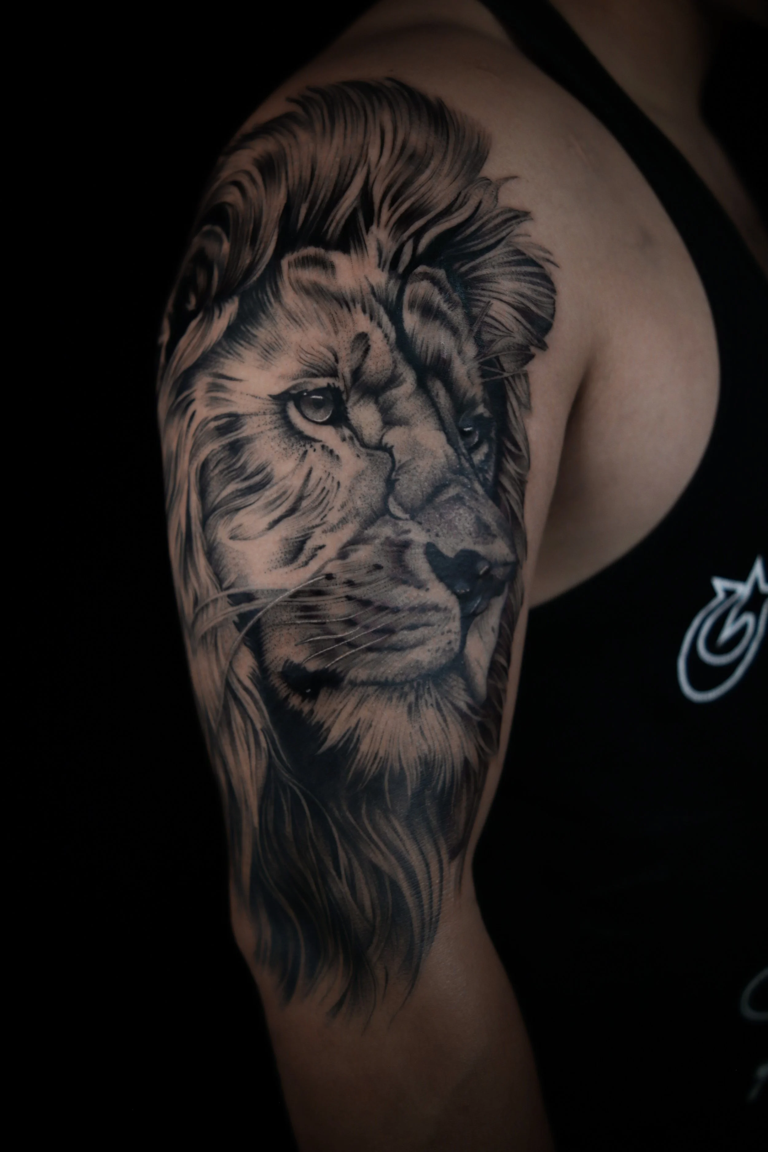 A detailed black and gray tattoo of a lion's face on a person's upper arm and shoulder.