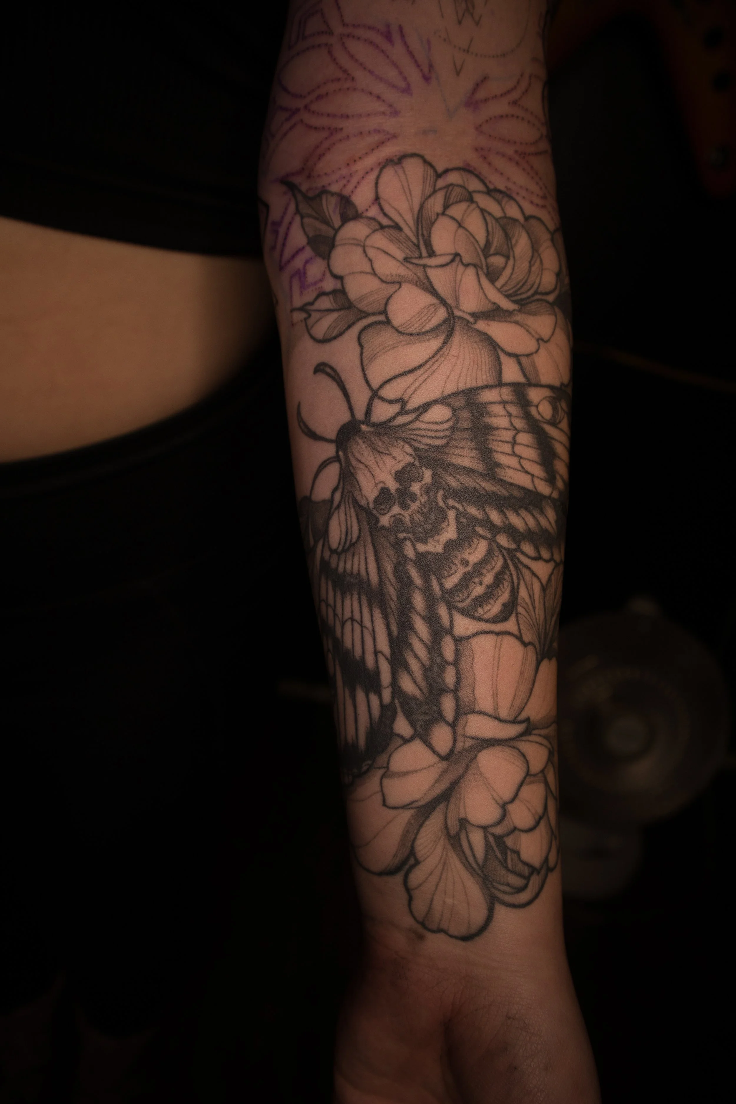 Tattoo of a butterfly, floral design, and a skull on person's forearm.