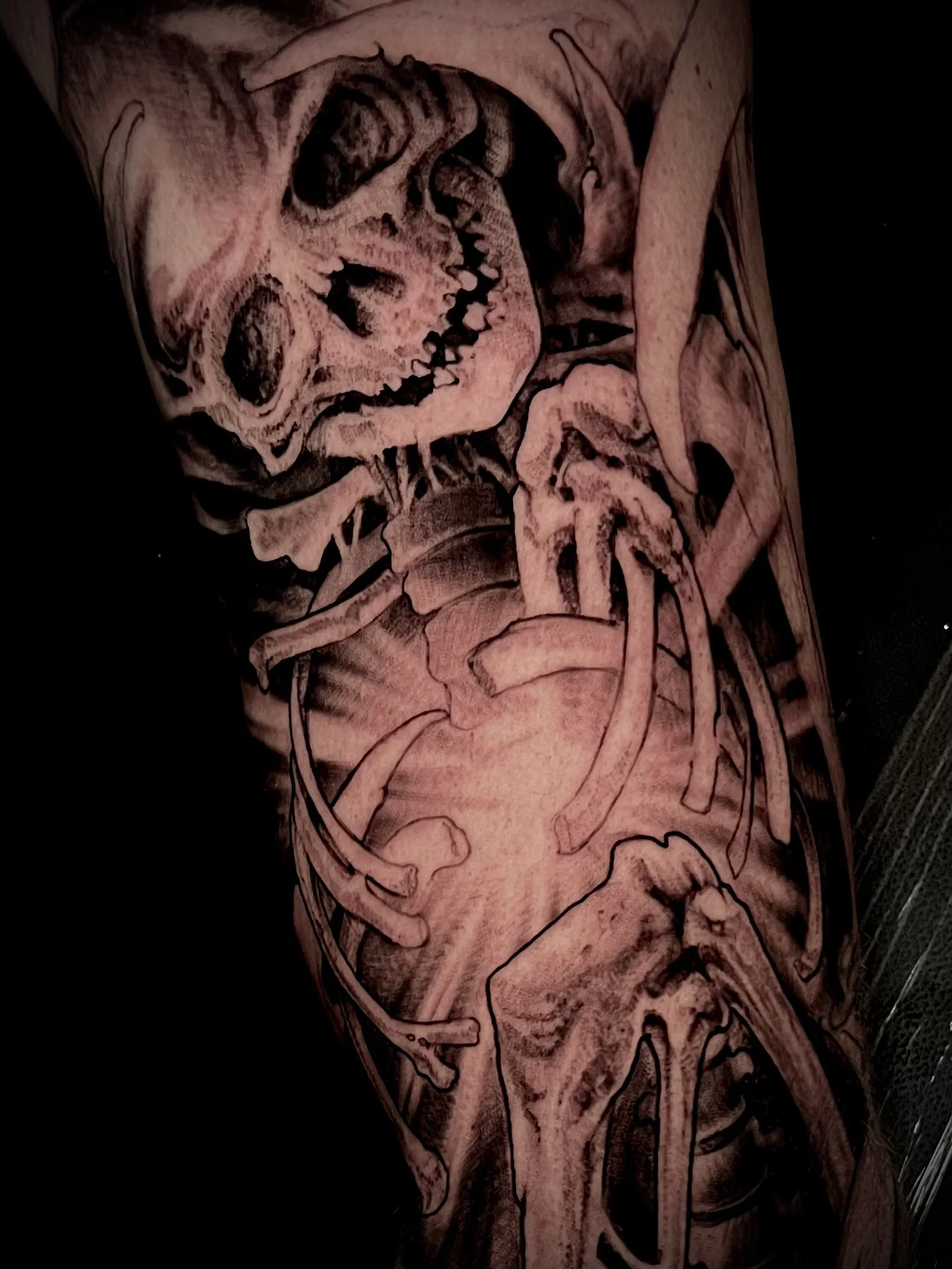 Black and grey tattoo of a skull and skeletal ribs on a person's arm.