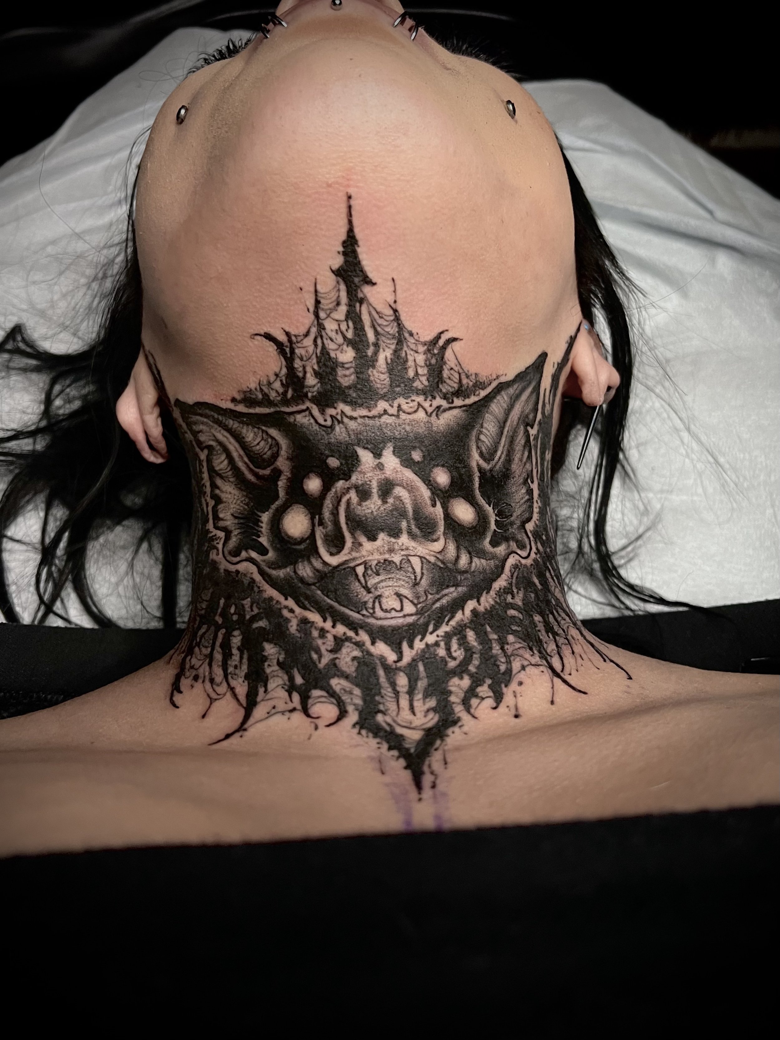Tattoo of a pig's face with pointed ears and fanged mouth on a person's neck, with a dark castle-like structure above it.