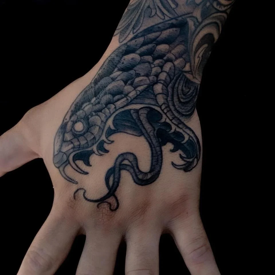 Tattoo of a sea serpent or dragon on a person's hand and wrist.