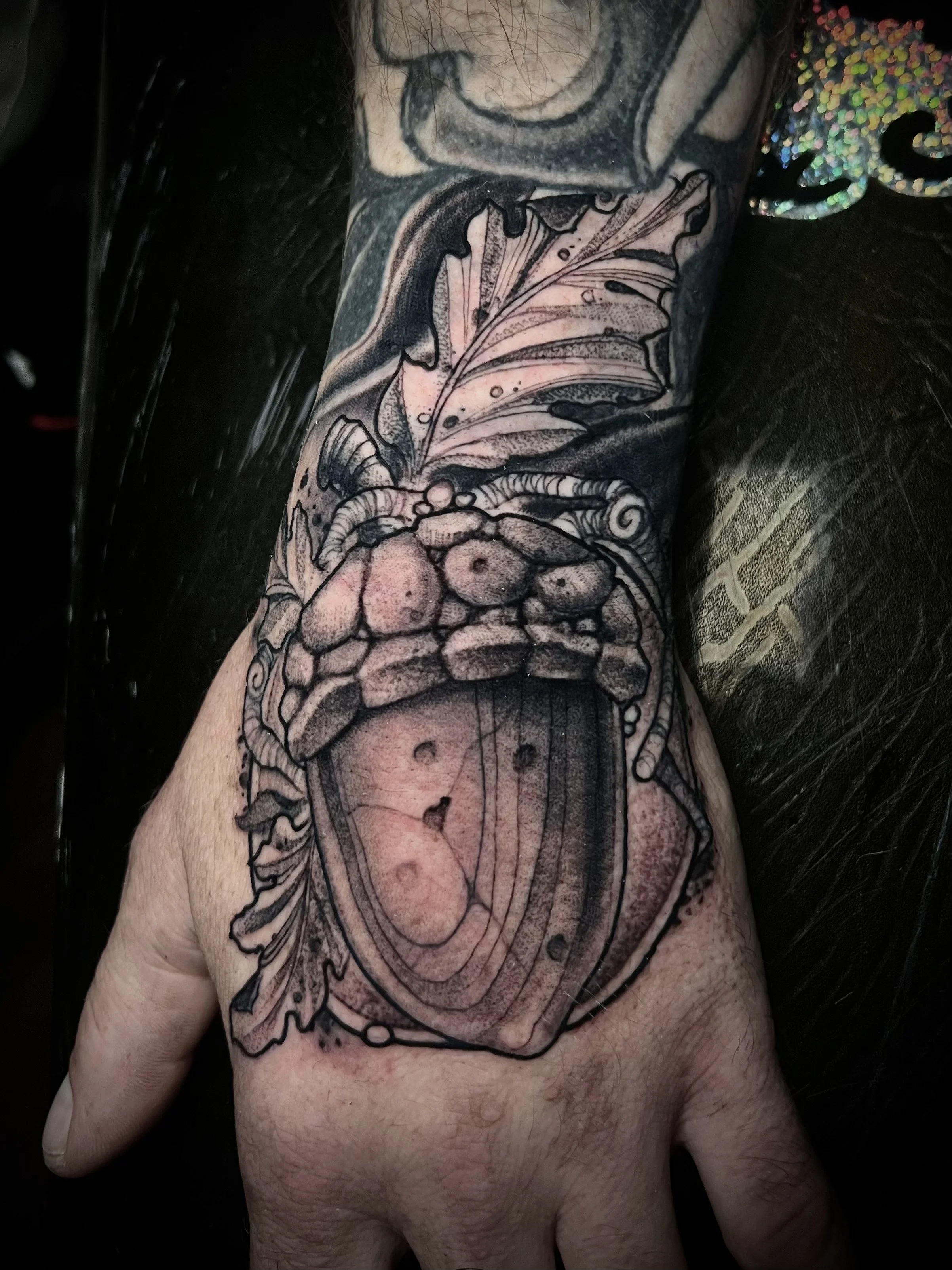 Black and gray tattoo of a large beetle with detailed antennae, wings, and body on a person's arm and hand.