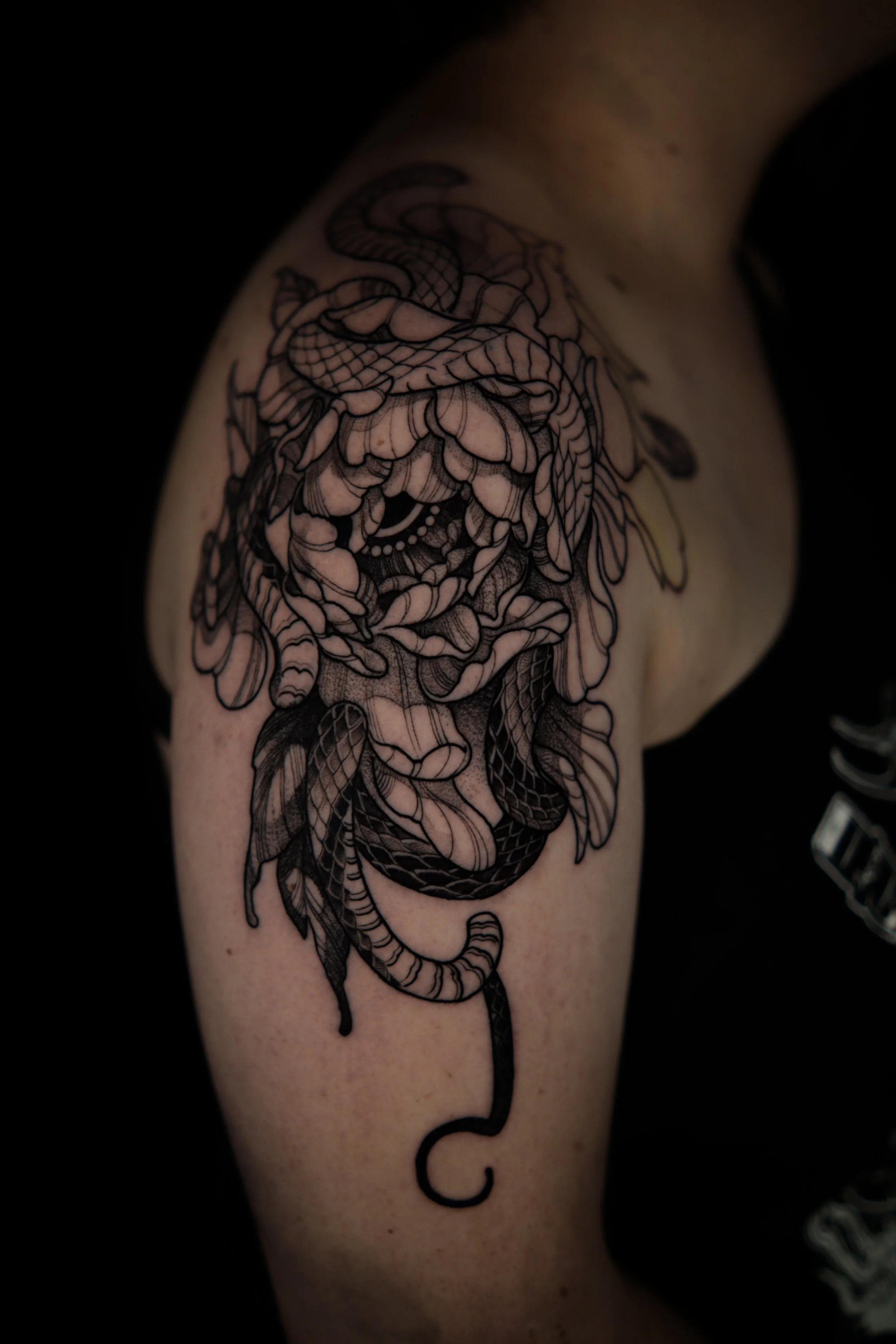 Tattoo of a lion's face with a snake entwined around it on a person's upper arm.