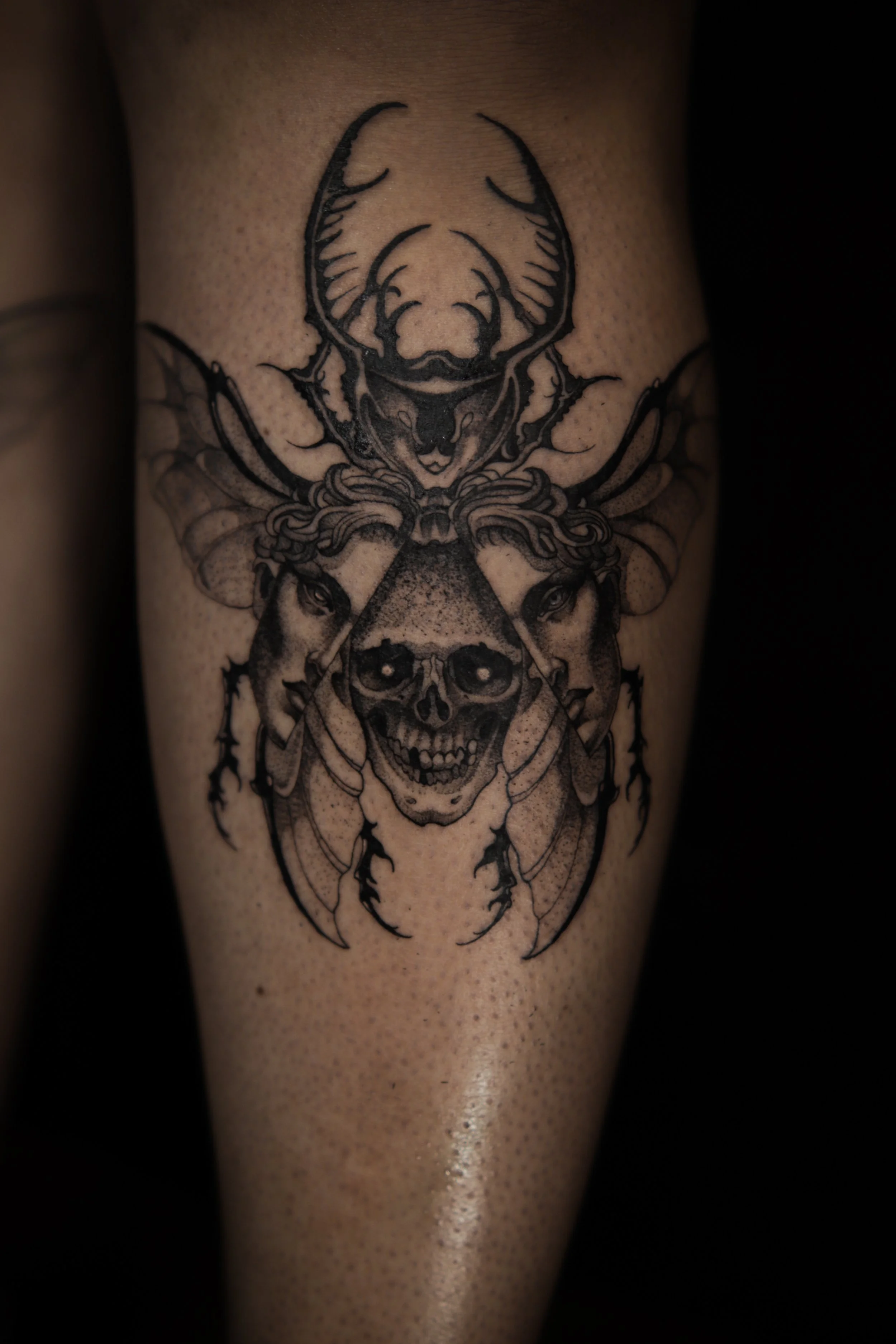 Black and gray tattoo of a skull, a stag, and a woman's face on a person's arm.