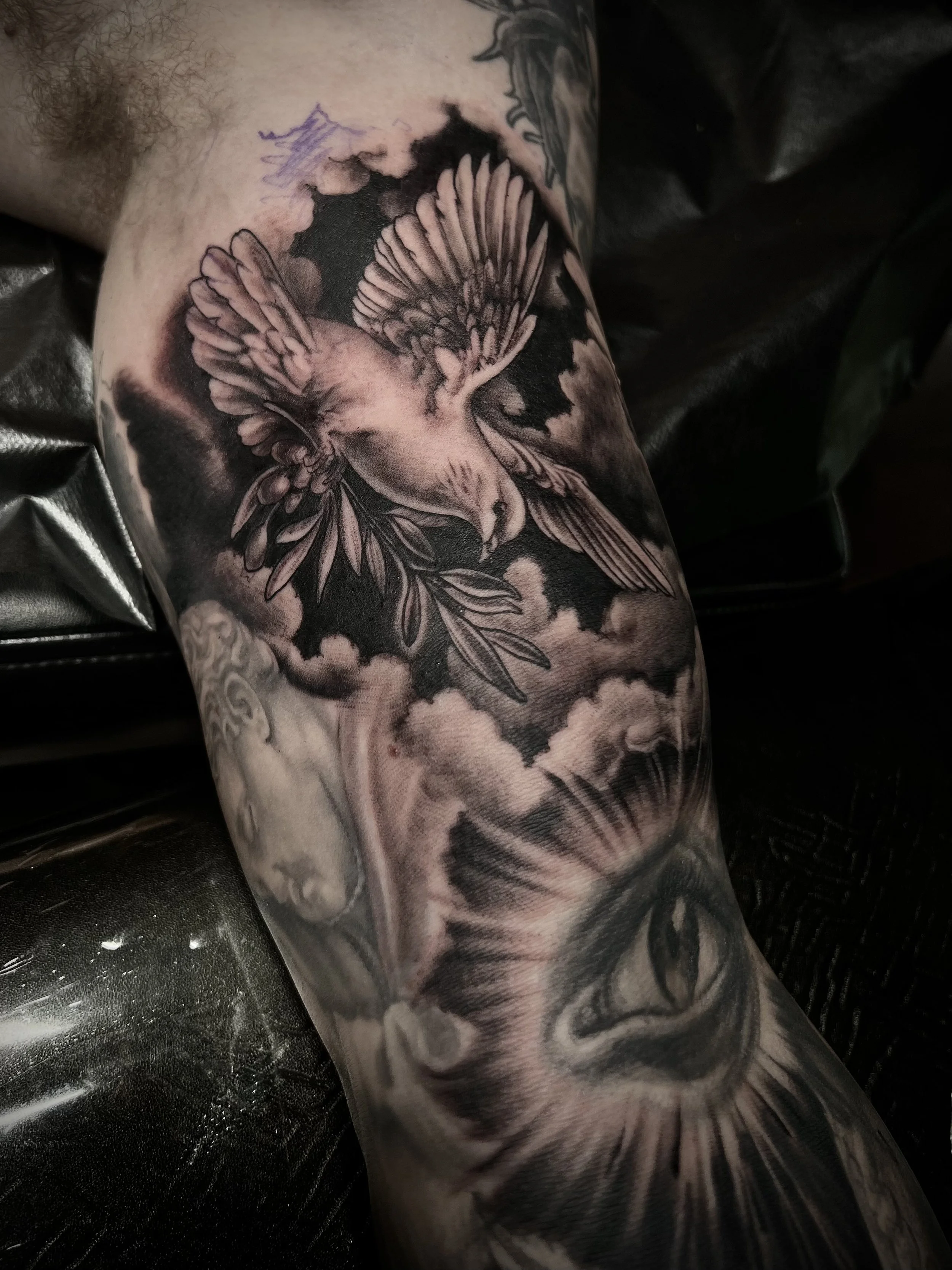 Black and gray tattoo of a bird flying among clouds on a person's arm, with a large eye below.