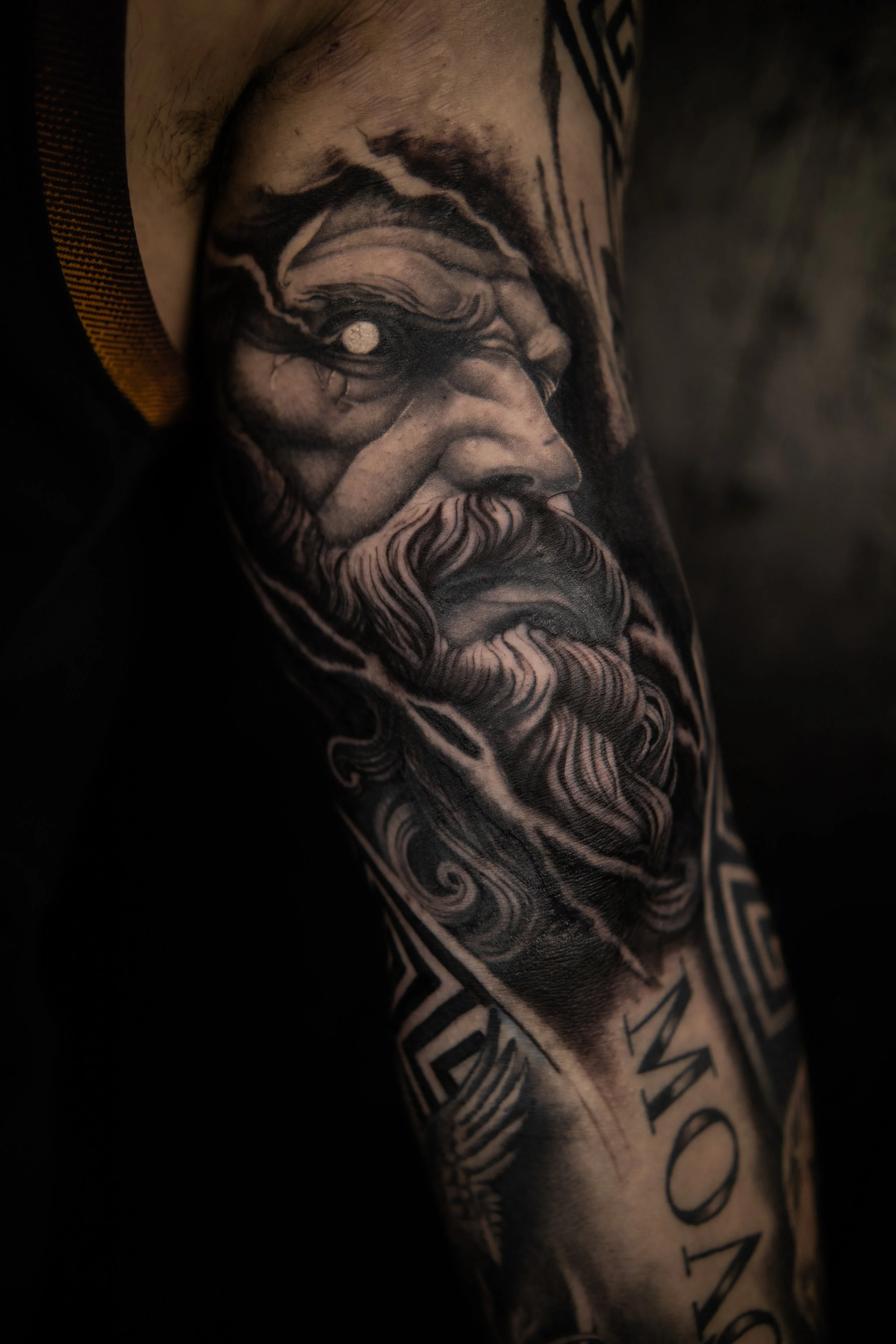 Close-up of a detailed black and gray tattoo of a bearded man's face on a person's arm.