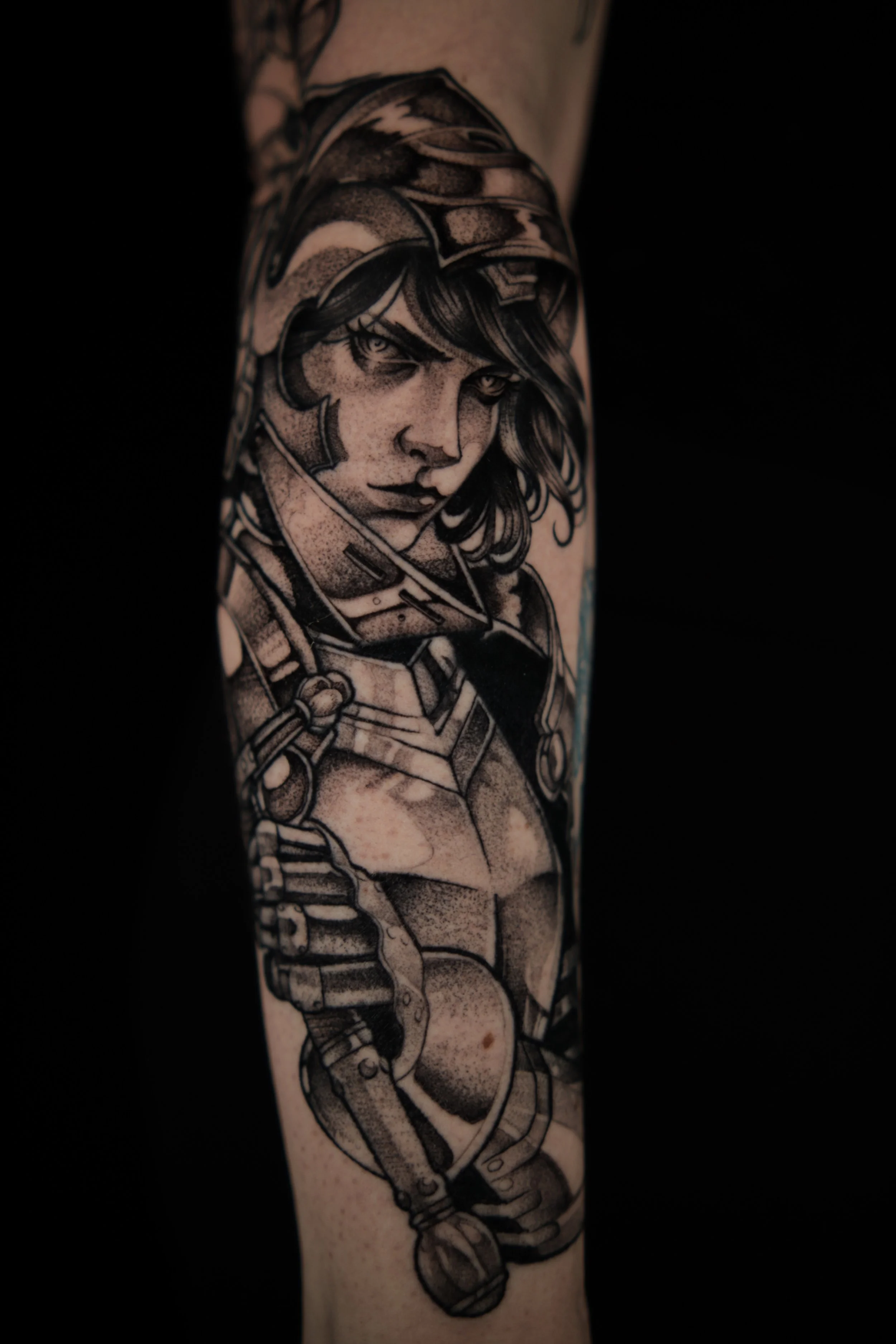 A black and gray tattoo of a female character in futuristic armor on someone's forearm.