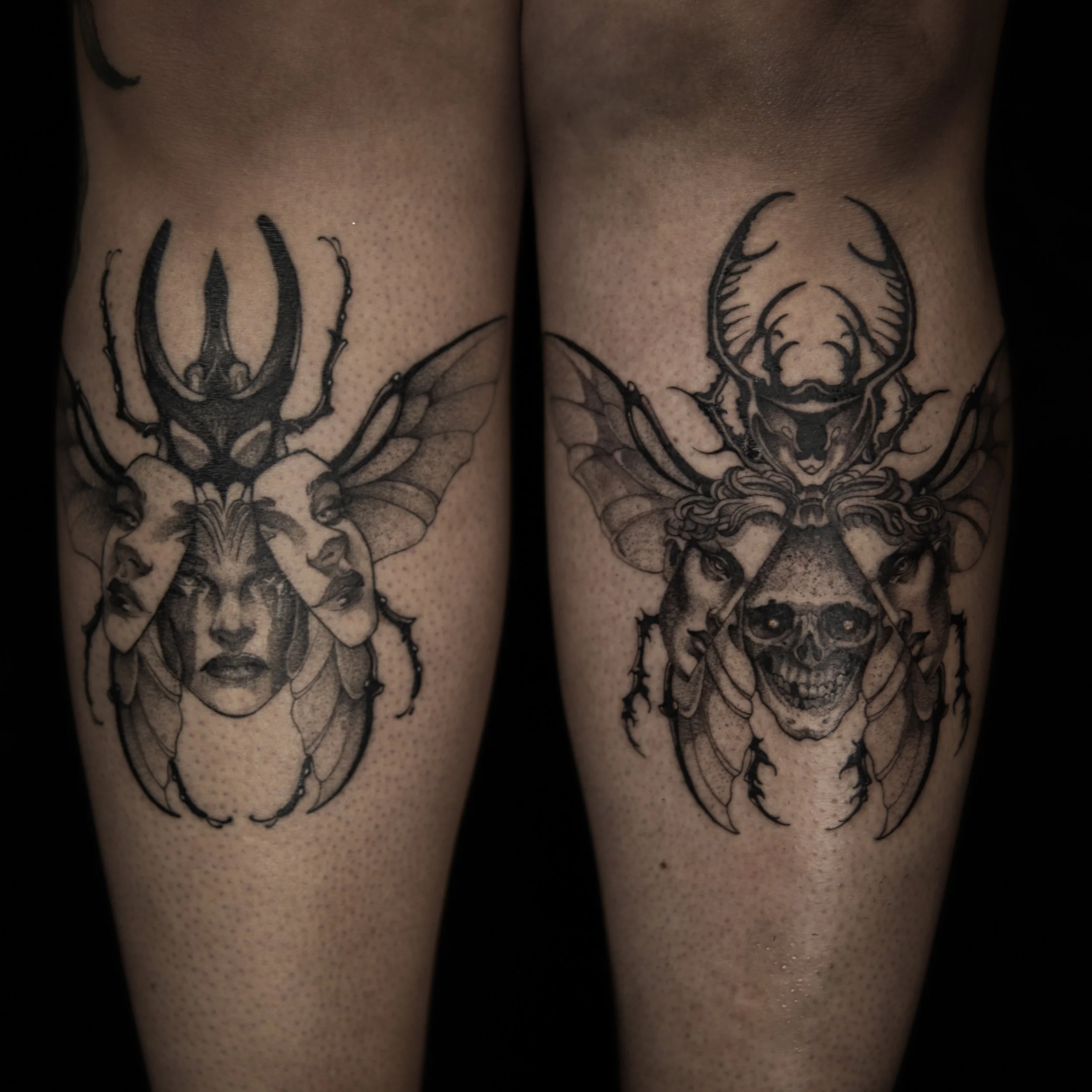 Black and grey tattoos of mythical creatures with human faces, insects, and skulls on two person's thighs.