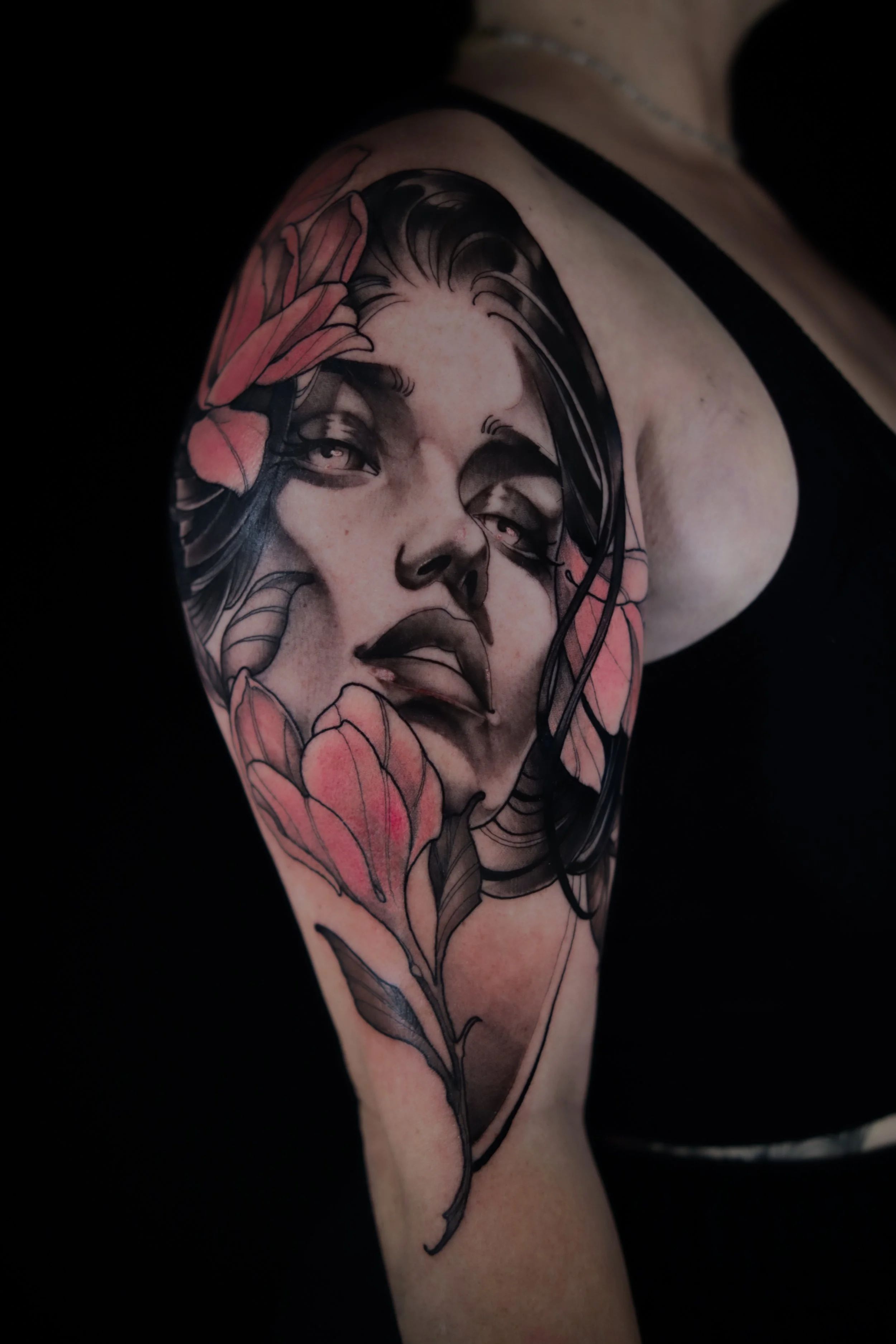 Black and gray tattoo of a woman's face with pink flowers on shoulder and upper arm.