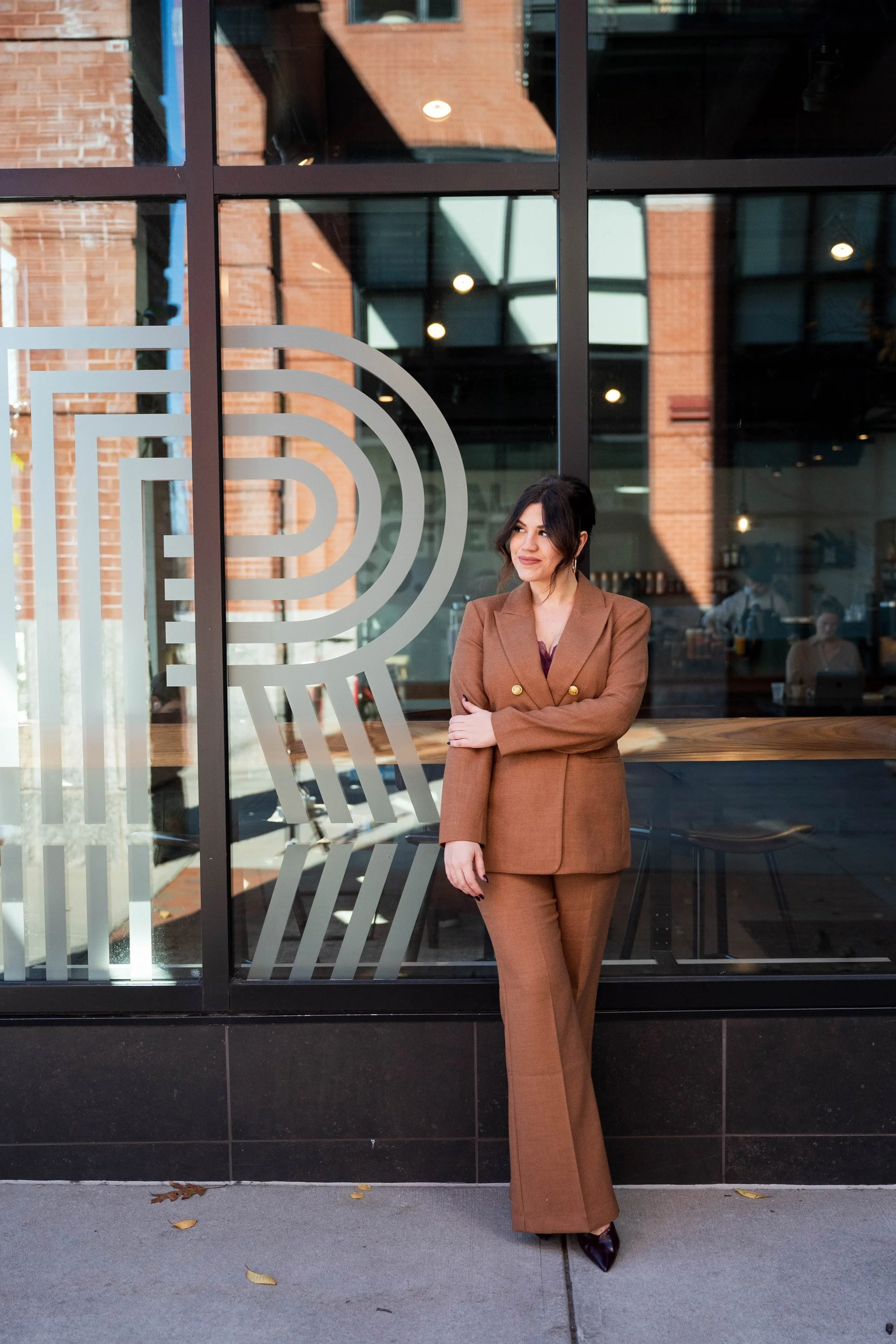 Anna Olsen, mental health professional, a woman in a brown suit standing outside a building with large glass windows and a partial logo on the window.