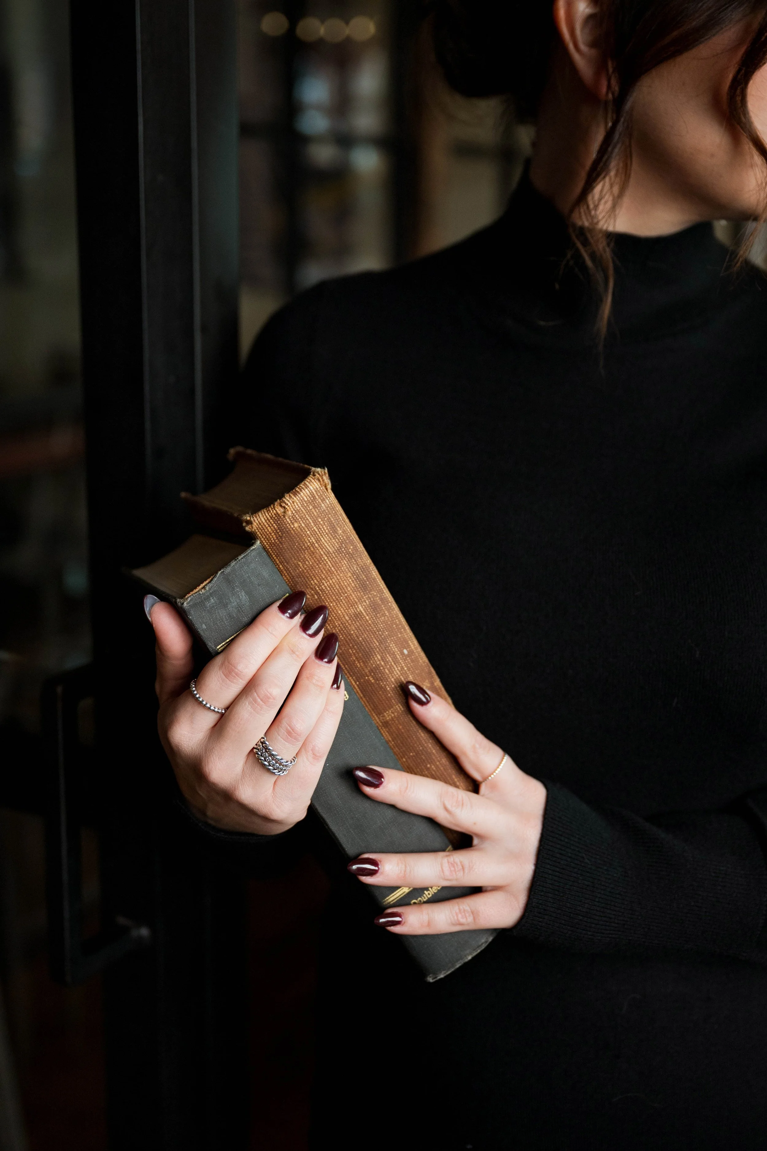 A woman in a black turtleneck holding a stack of old, worn books.