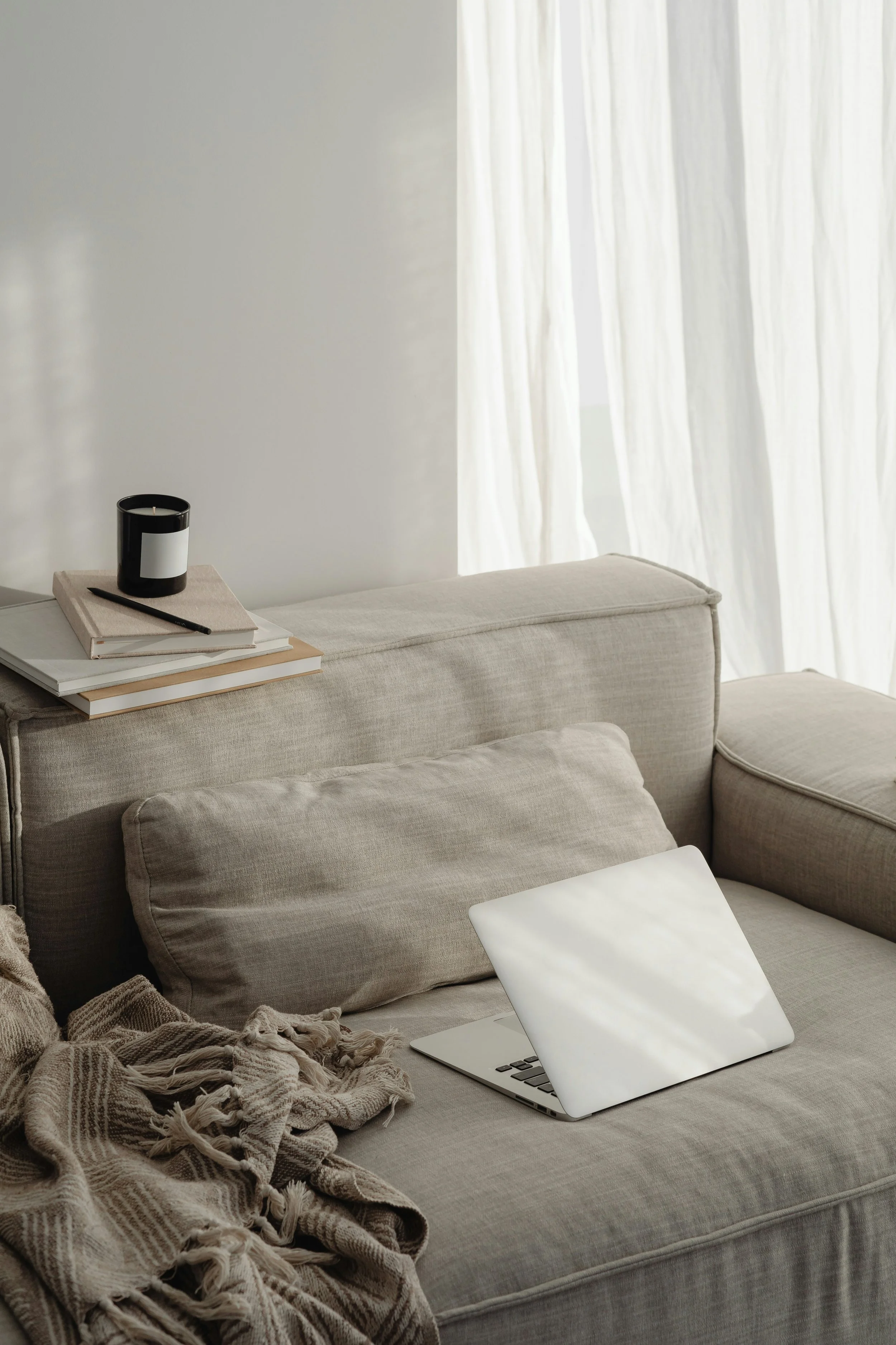 A beige loveseat with a blanket, computer, candles, and books