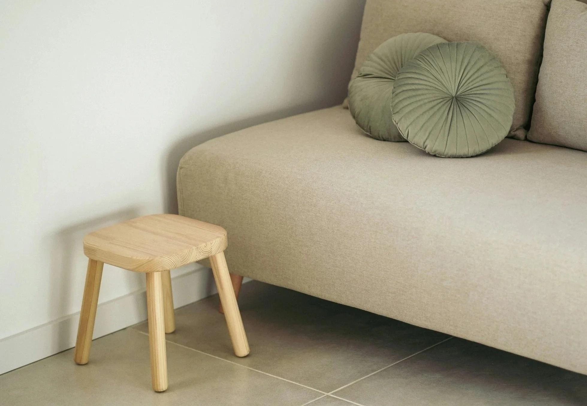 A cream couch with green pillows, next to a short wooden stool