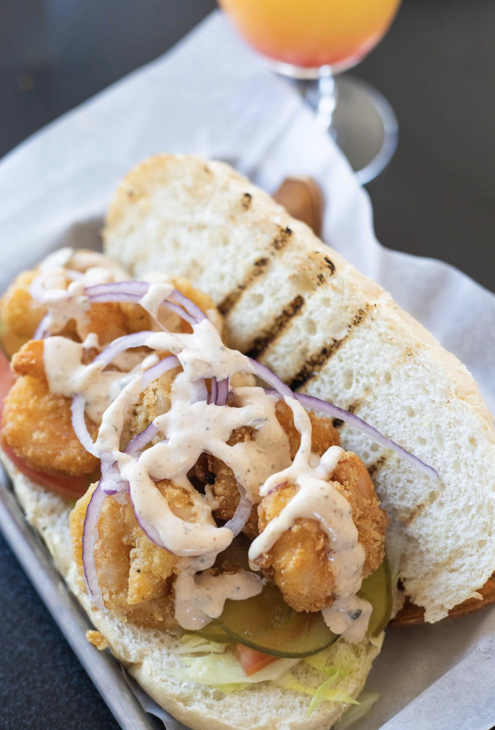 A shrimp poboy is pictured with crispy shrimp on a toasted hoagie topped with remoulade sauce.