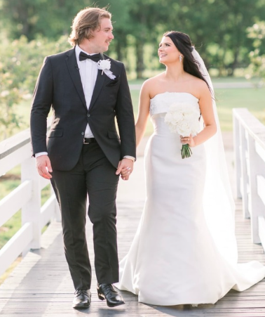 Bride and groom walking on a bridge outdoors on their wedding day, smiling at each other.