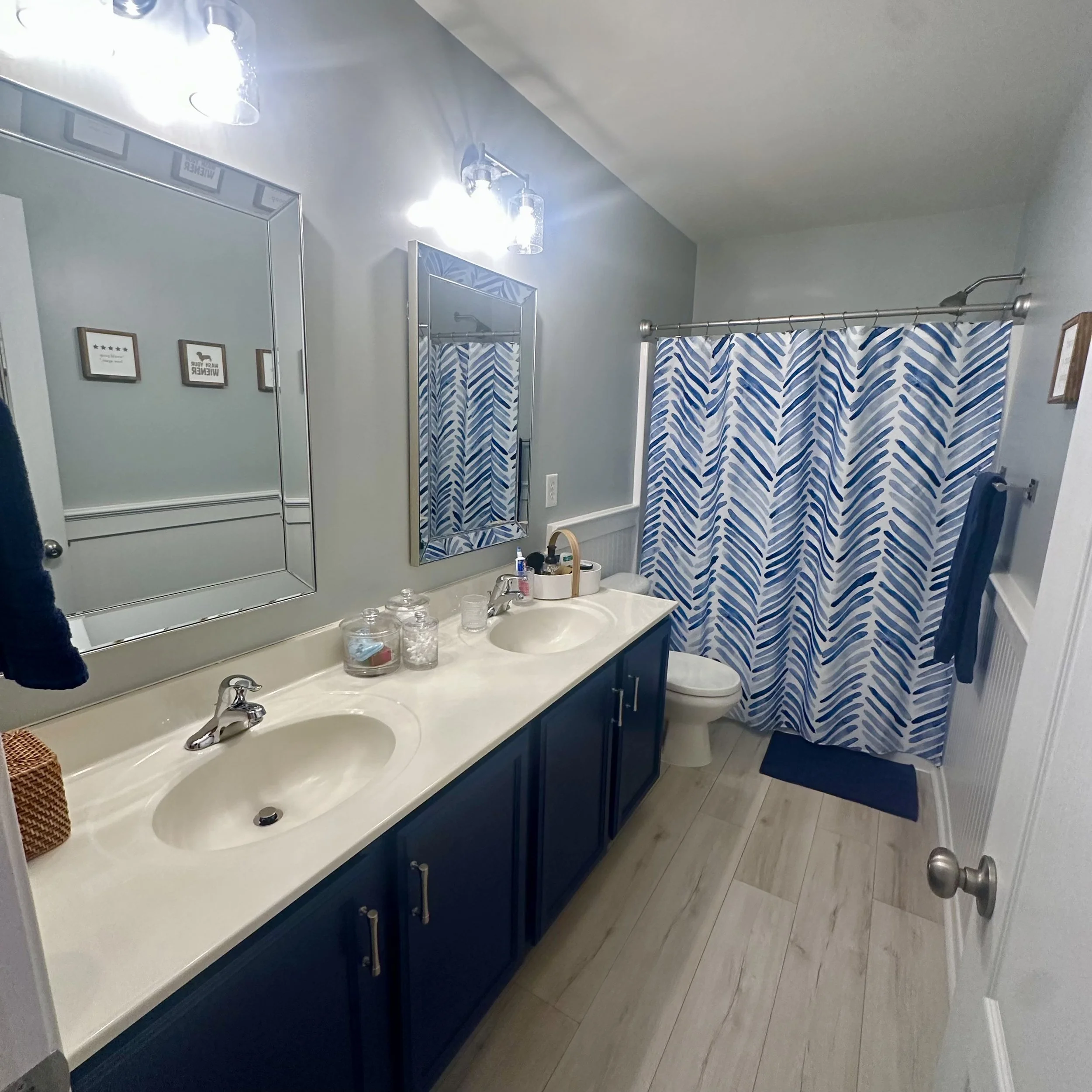 Bathroom with dual sinks, large mirror, blue cabinet, and a shower with blue and white patterned curtain.