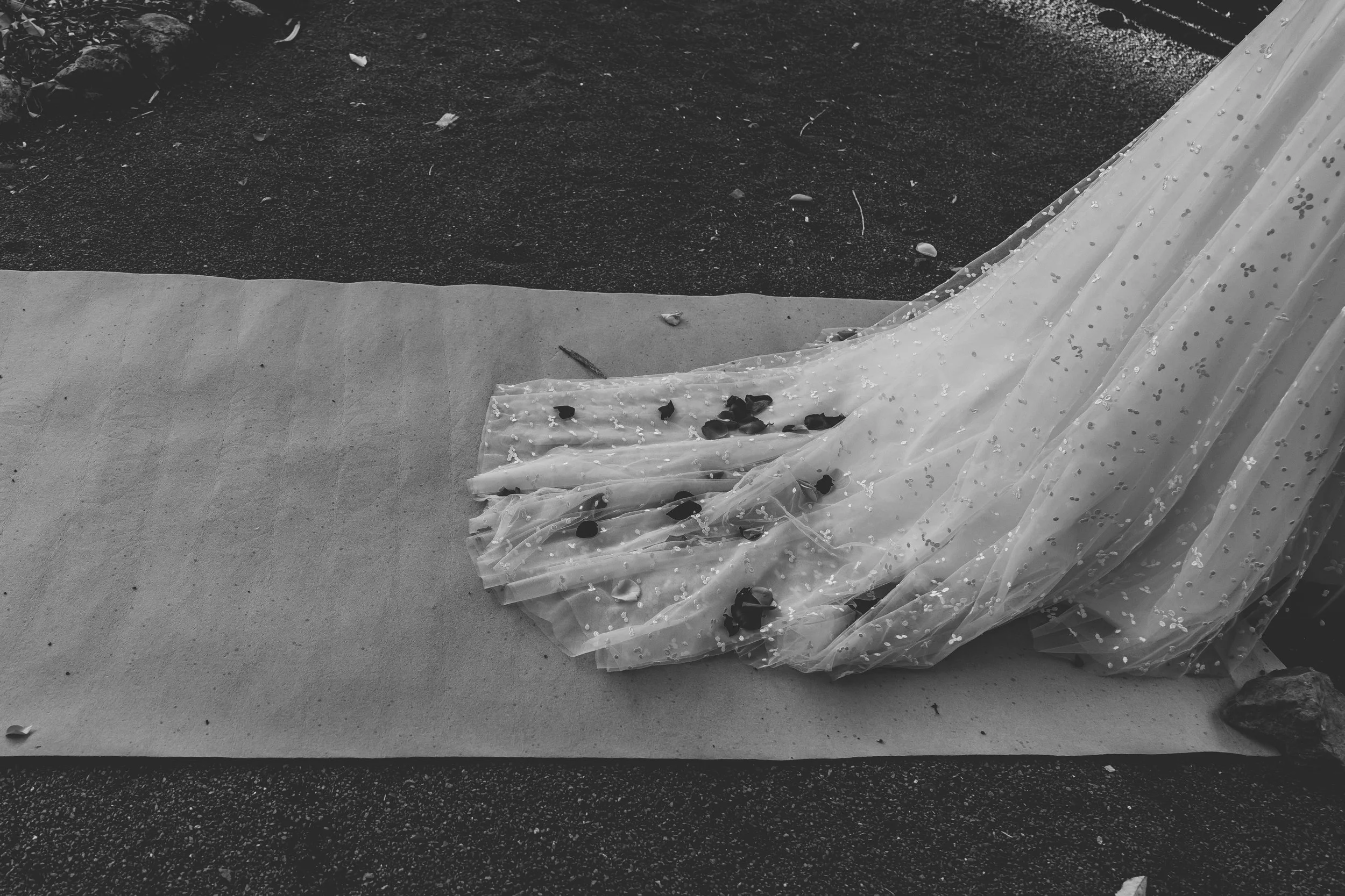 A wedding dress laying on the ground with dark spots and debris around, on a black and gray surface.