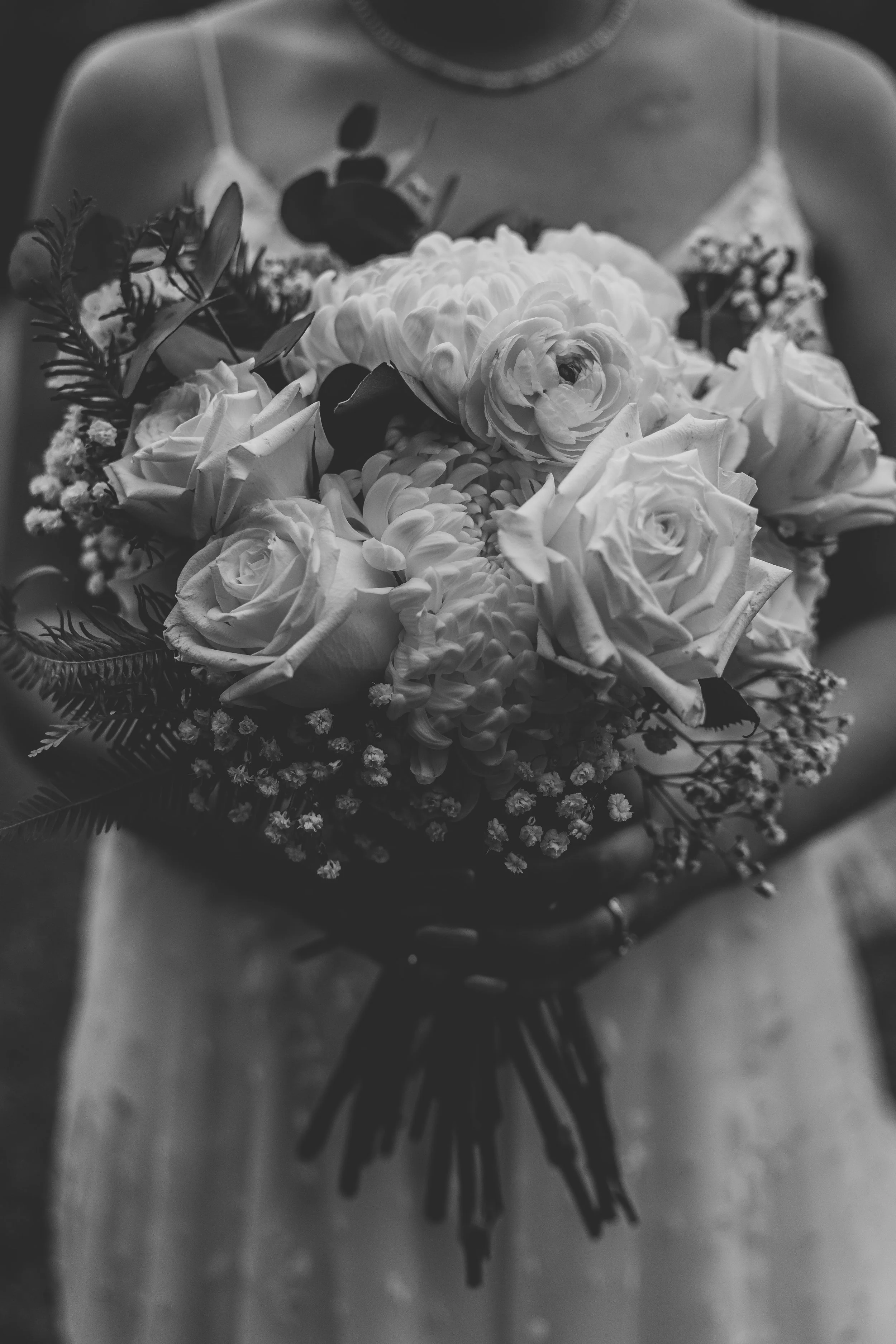Black and white photograph of a woman holding a bouquet of flowers, including roses and other blooms, with her body partially visible and her face not shown.