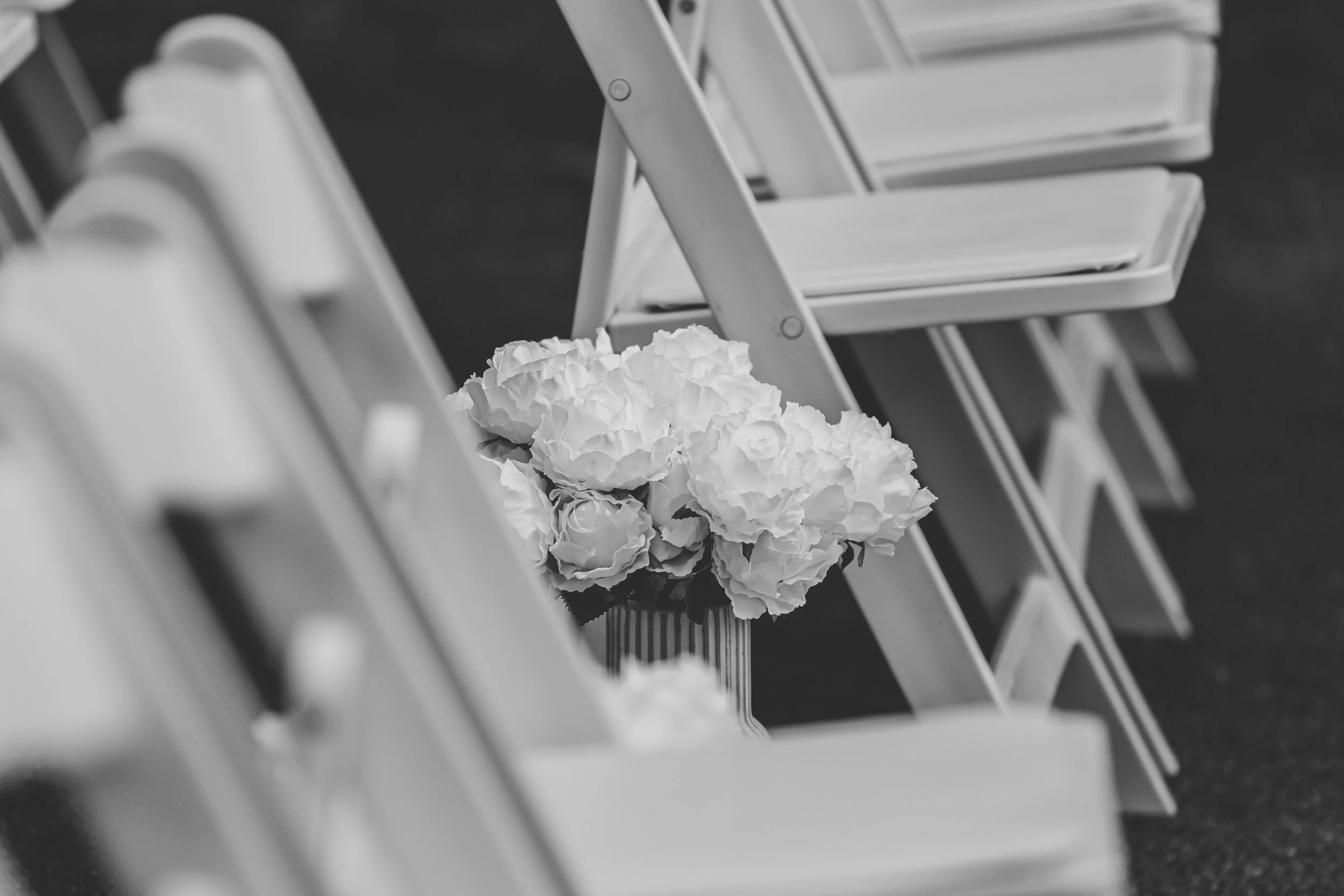 A bouquet of flowers in a vase placed among empty white folding chairs.