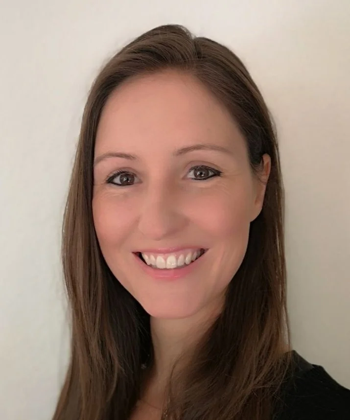 Lächelnde Frau mit braunen Haaren vor hellem Hintergrund.