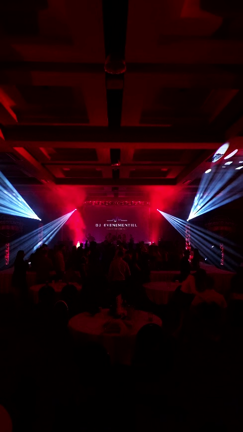 Scène de concert ou de fête avec des éclairages colorés et des silhouettes de personnes dans une salle avec un plafond décoratif.