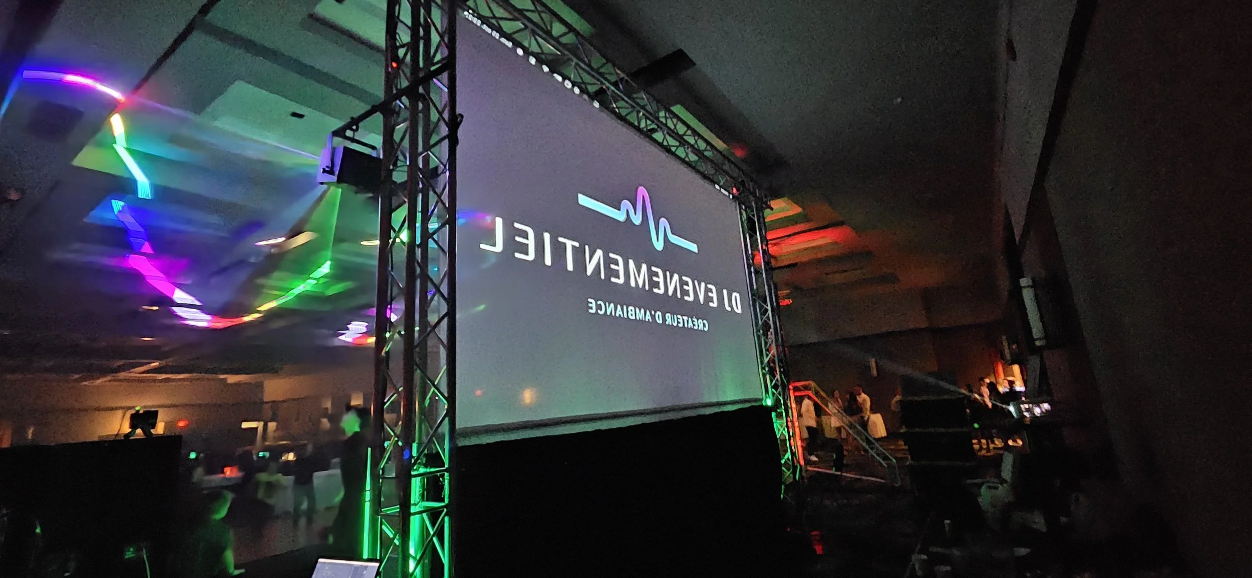 Une grande scène avec un écran d'événement de santé dénommé "Deevenement" avec un logo de cœur en forme de ligne ECG en haut de l'écran. L'environnement est sombre avec des lumières colorées et quelques personnes en arrière-plan.