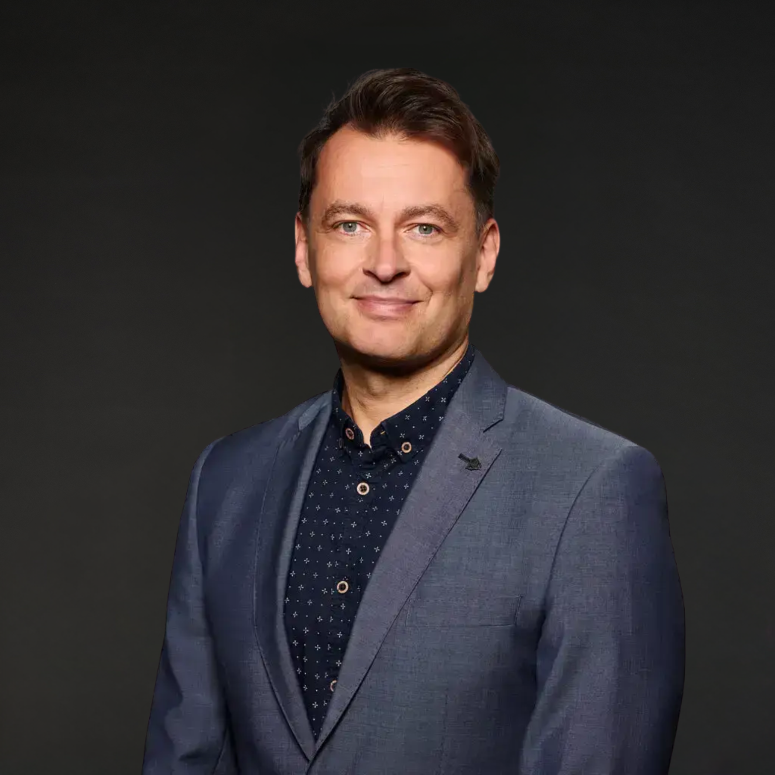 Porträt eines Mannes in einem blauen Anzug vor dunklem Hintergrund.