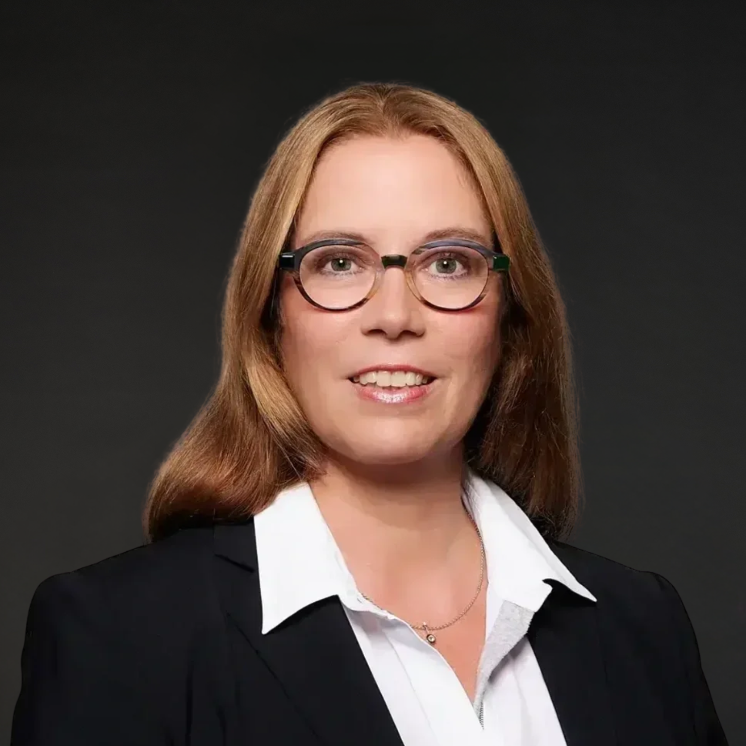 Porträt einer Frau mit Brille in formeller Kleidung vor dunklem Hintergrund.