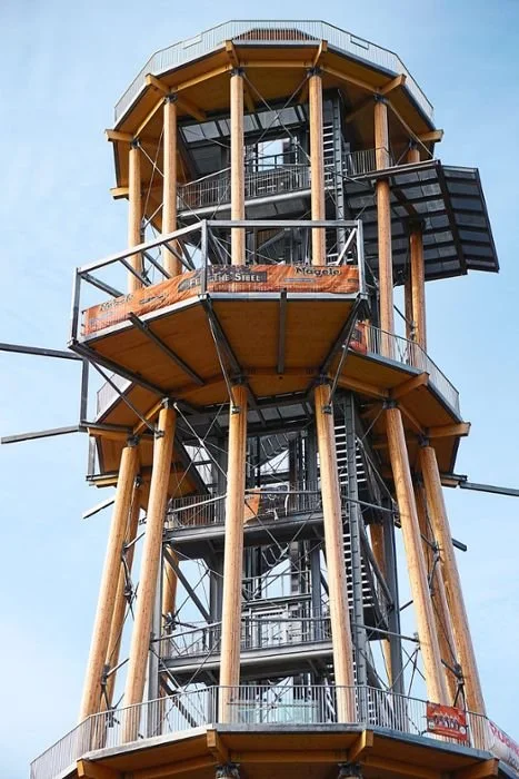 Mehrstöckige Aussichtsplattform mit Holzstützen und Glasfenstern, aus Blick Richtung Himmel.