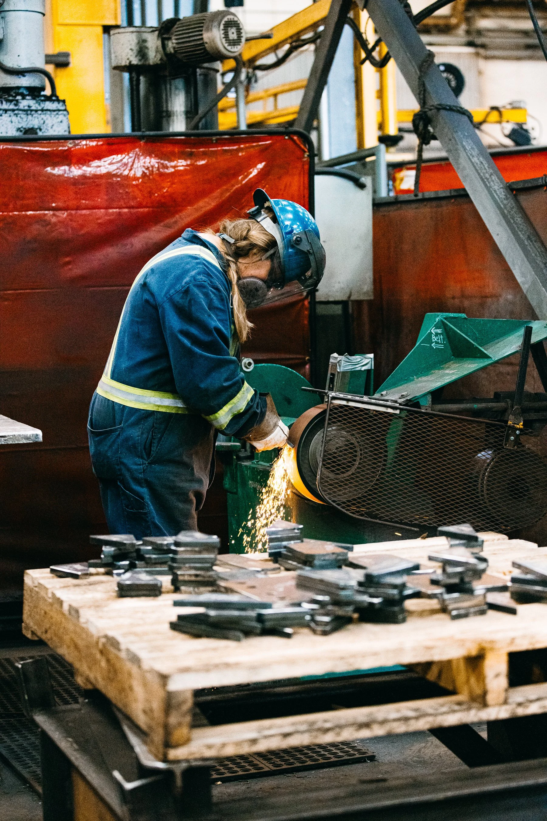 A worker using a grinding machine to cut metal, with sparks flying, in an industrial workshop setting.