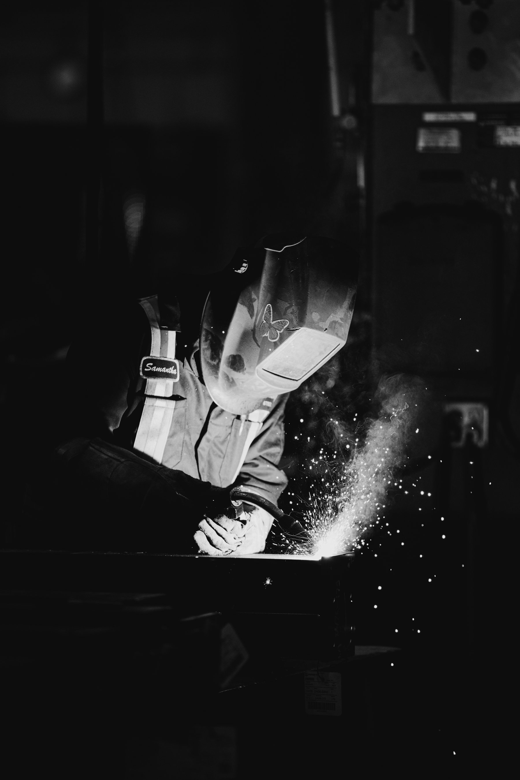 A person welding in a workshop, wearing protective gear, with bright sparks flying from the welding process.